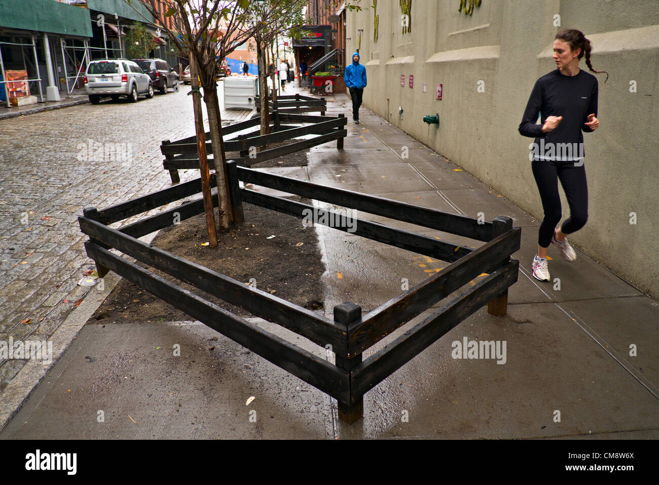 October 30, 2012, Brooklyn, NY, US.  On the morning after Hurricane Sandy struck New York City, a woman jogs past trees whose fences were tossed around by floodwaters. Credit:  Joseph Reid / Alamy Live News Stock Photo