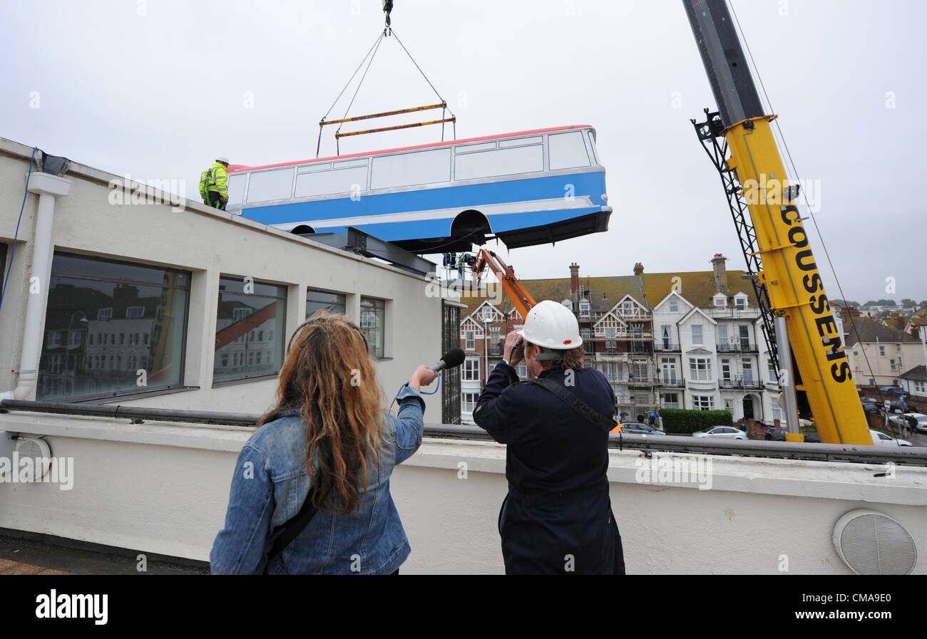 A coach is hoisted by crane on to the roof of the De La Warr Pavilion Bexhill today as part of artist Richard Wilson's art installation Hang on lads I've Got an Idea based on The Italian Job cliff edge sceneJuly 2012 Stock Photo
