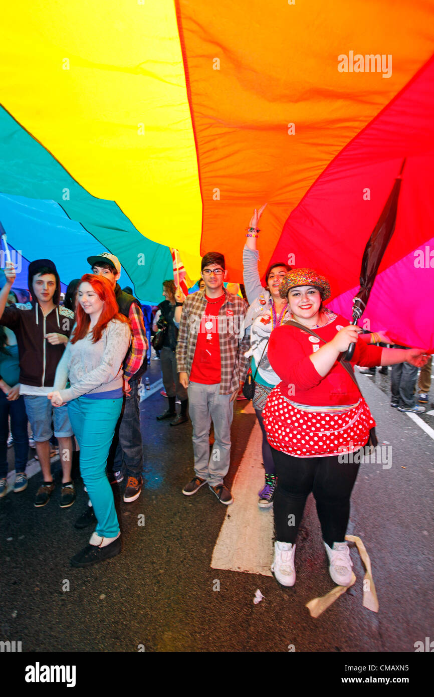London, UK. 7th July 2012. Participants sheltering from the rain under the rainbow flag marching in World Pride 2012, London, England Stock Photo