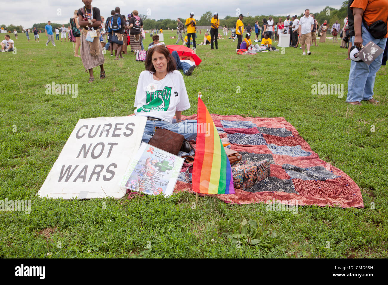A woman rests while displaying a sign and a rainbow flag, as she waits for the AIDS march in Washington, DC to start - July 22, 2012, Washington, DC USA Stock Photo