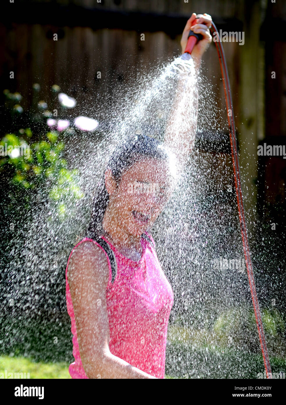 Brighton UK  - Young woman hoses herself down with the garden sprinkler after her early morning run Stock Photo