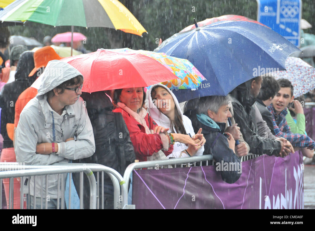 Hyde Park Corner, London, UK. 29th July 2012. The crowd try to stay dry as they watch the women's cycling road race at Hyde Park Corner as the race approaches the end as the riders and crowd endure heavy rain and a thunderstorm. Stock Photo