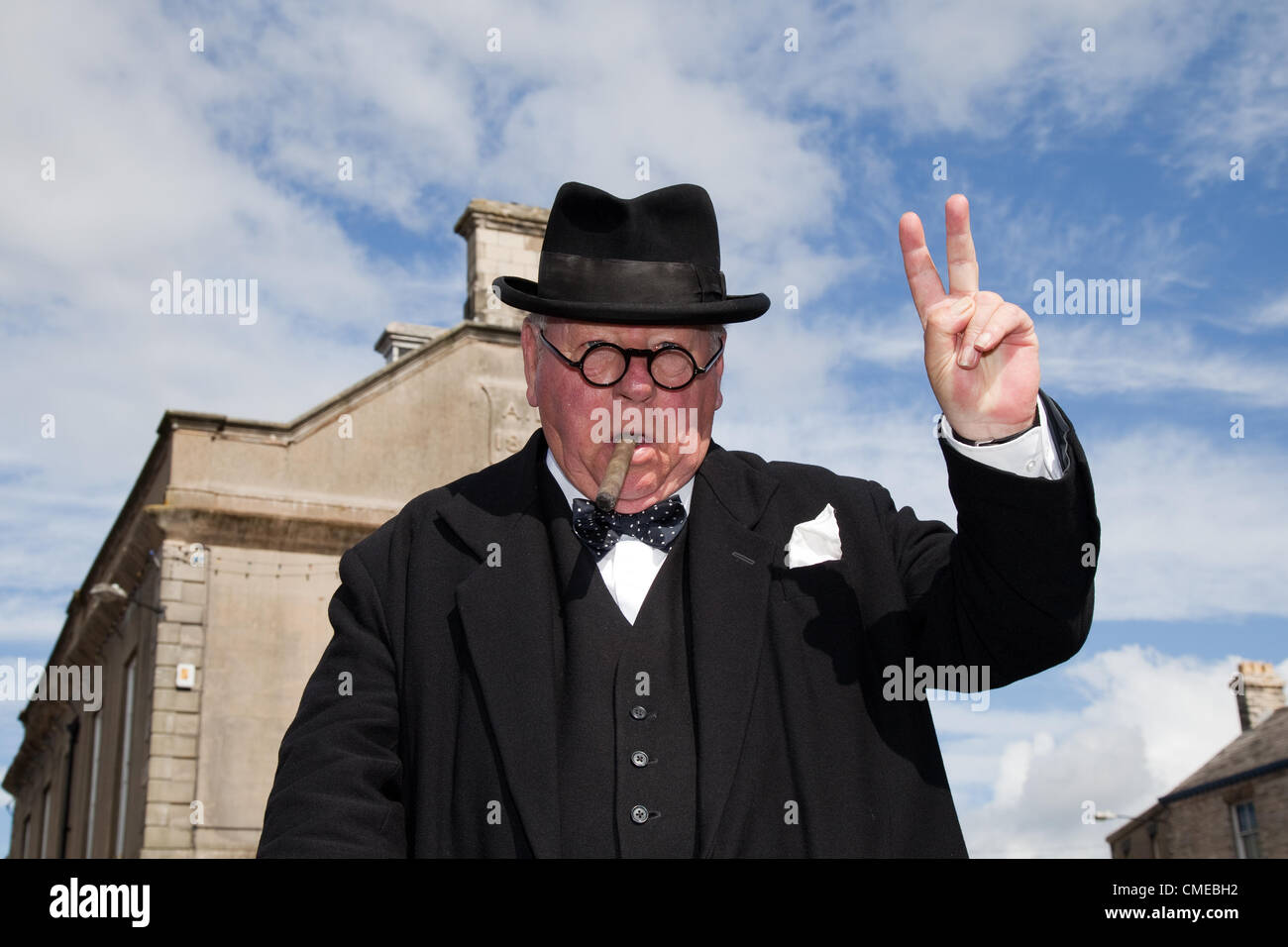 Peter Austwick, (MR) look-alike, double, or doppelgänger from Peterborough,  a 1940s Churchill lookalike, V-sign, V-for-Victory sign with two fingers, actor, people, event, man, veteran, city, male, performance, show, army, history, military, soldier, uniform, vintage, war, historical, ii, perform, person, re-enactment, building at the market place Leyburn   One of the biggest events in Leyburn's calender the 1940s World War II, Wartime Re-enactment Weekend, a summer event on July 28th & 29th 2012, Wensleydale,  North Yorkshire Dales, Richmondshire, UK Stock Photo