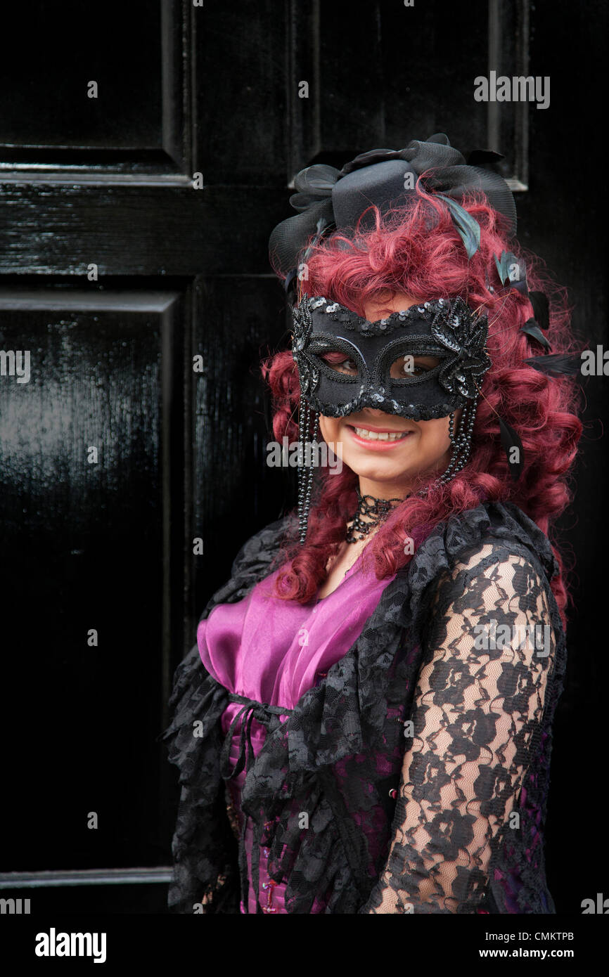 Woman. girl wearing purple goth costume with eye mask Whitby, Yorkshire, 2013. Trinity Stark, wearing fancy dress, a mask and red wig at the UK'S Biggest Goth & Alternative Weekend. Whitby. Goths, romantics and macabre fans at the Whitby Goth Weekend, which has become their spiritual home. As well as Goths, there are all manner of weird and wonderful characters with faces obscured at the Halloween Special  founded by Jo Hampshire in 1994. Stock Photo