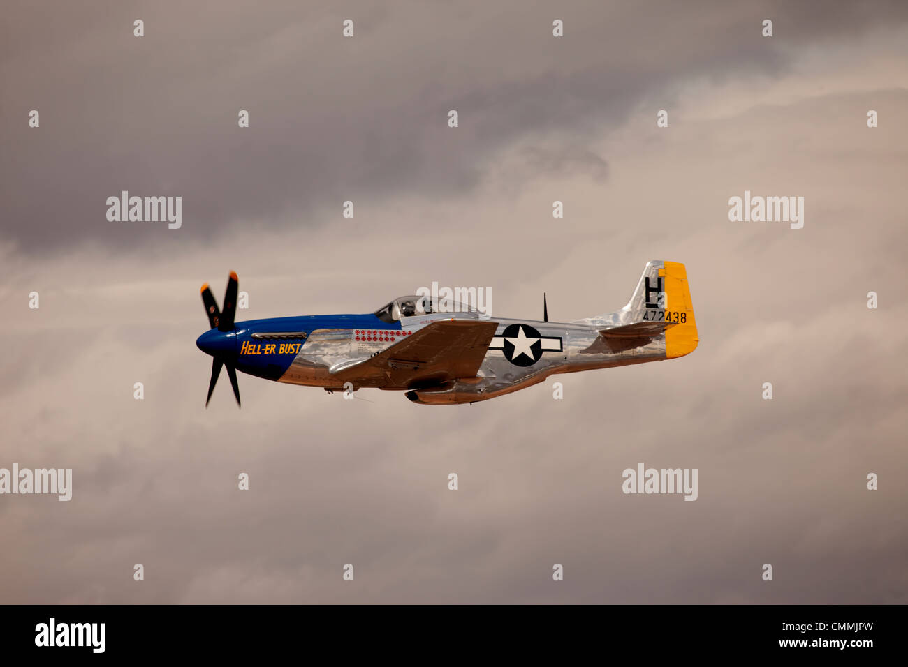Fly by of P-51 Mustang air superiority fighter from World War II. Nose art Heller Bust. Flight with storm clouds. Stock Photo