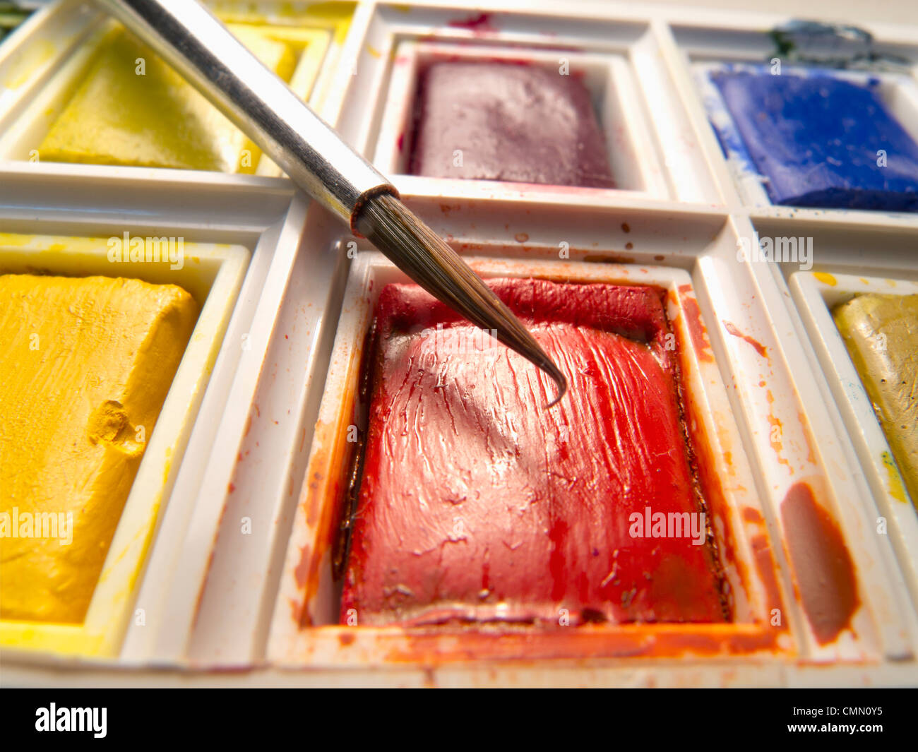 Closeup of brush poised above tablet of red water colour in a paint box. Stock Photo