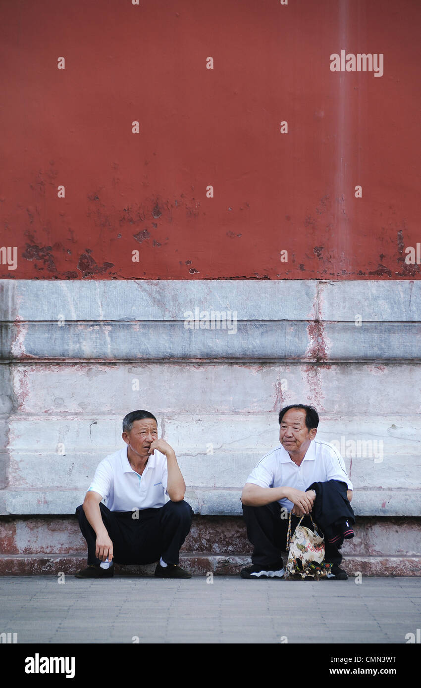 Two male Chinese tourists looking tired at the Forbidden City, Beijing, here demonstrating the famous 'Chinese Squat'. Stock Photo