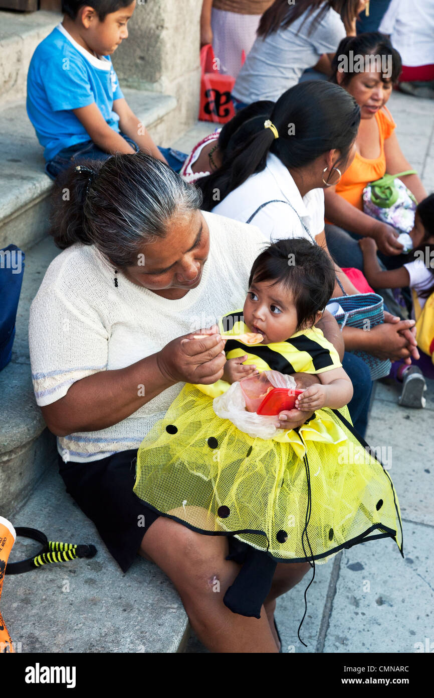 loving grandmother feeds baby granddaughter dressed as worker bee before march Alcala to Zocalo to celebrate microfinance lender Stock Photo