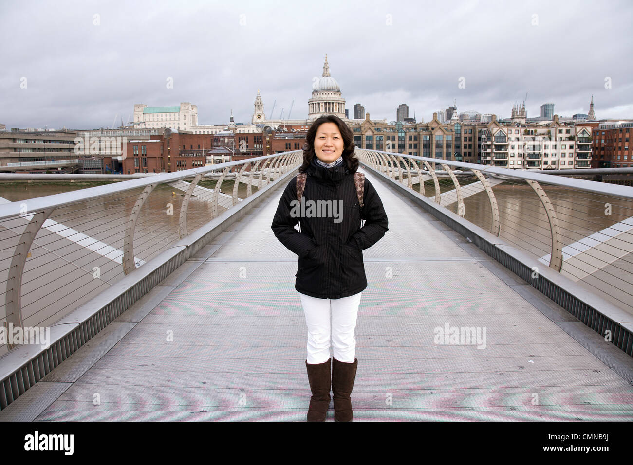 Smiling East Asian Woman at Millennium Bridge, St Paul's Cathedral in the distance. Stock Photo