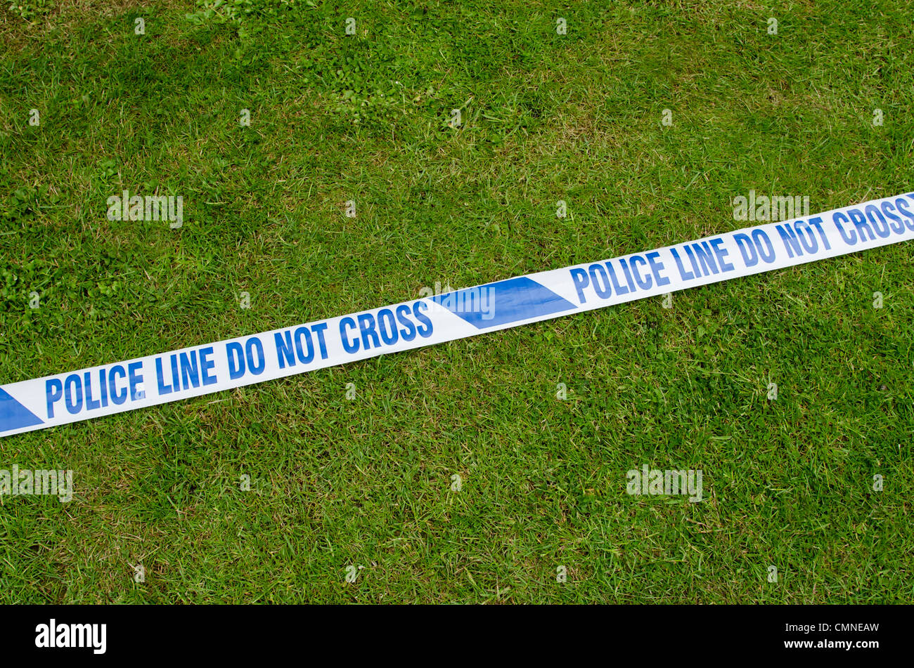 White tape with 'Police Line Do Not Cross' printed on it laying on the grass. Stock Photo