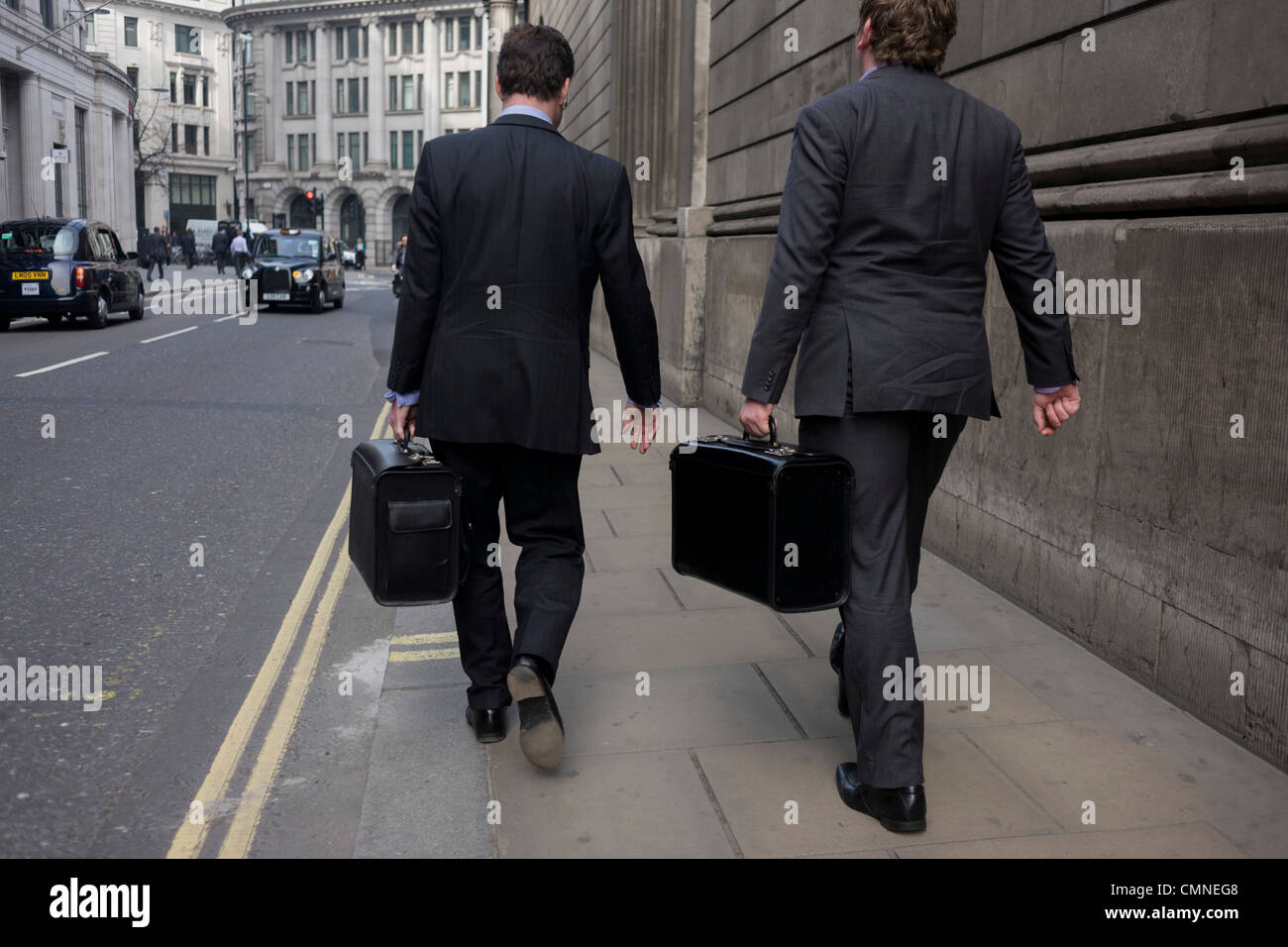 Two city businessmen walk along a financial district street each carrying identical briefcases. Stock Photo