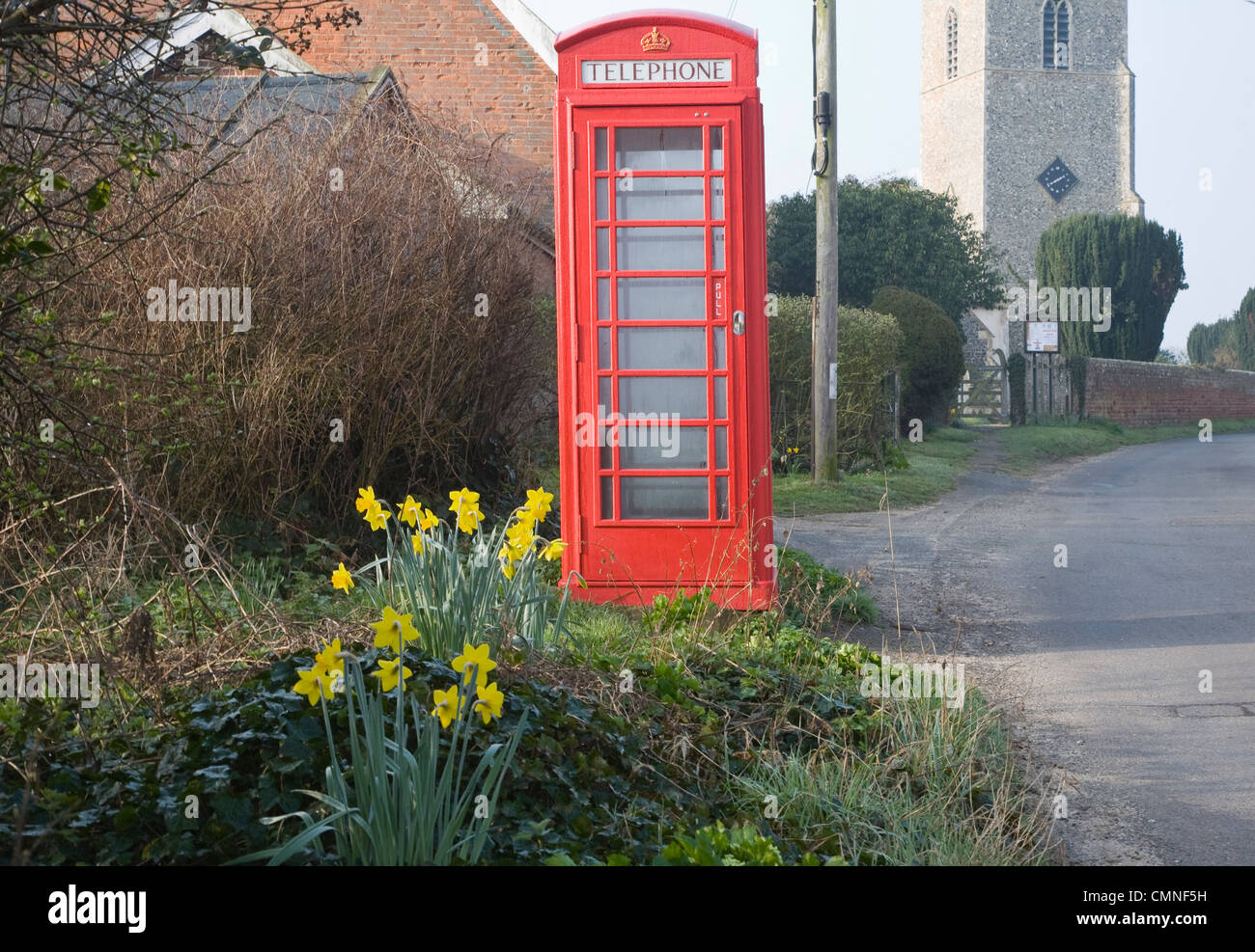Red traditional telephone box daffodils village street with church, Great Glemham, Suffolk, England Stock Photo
