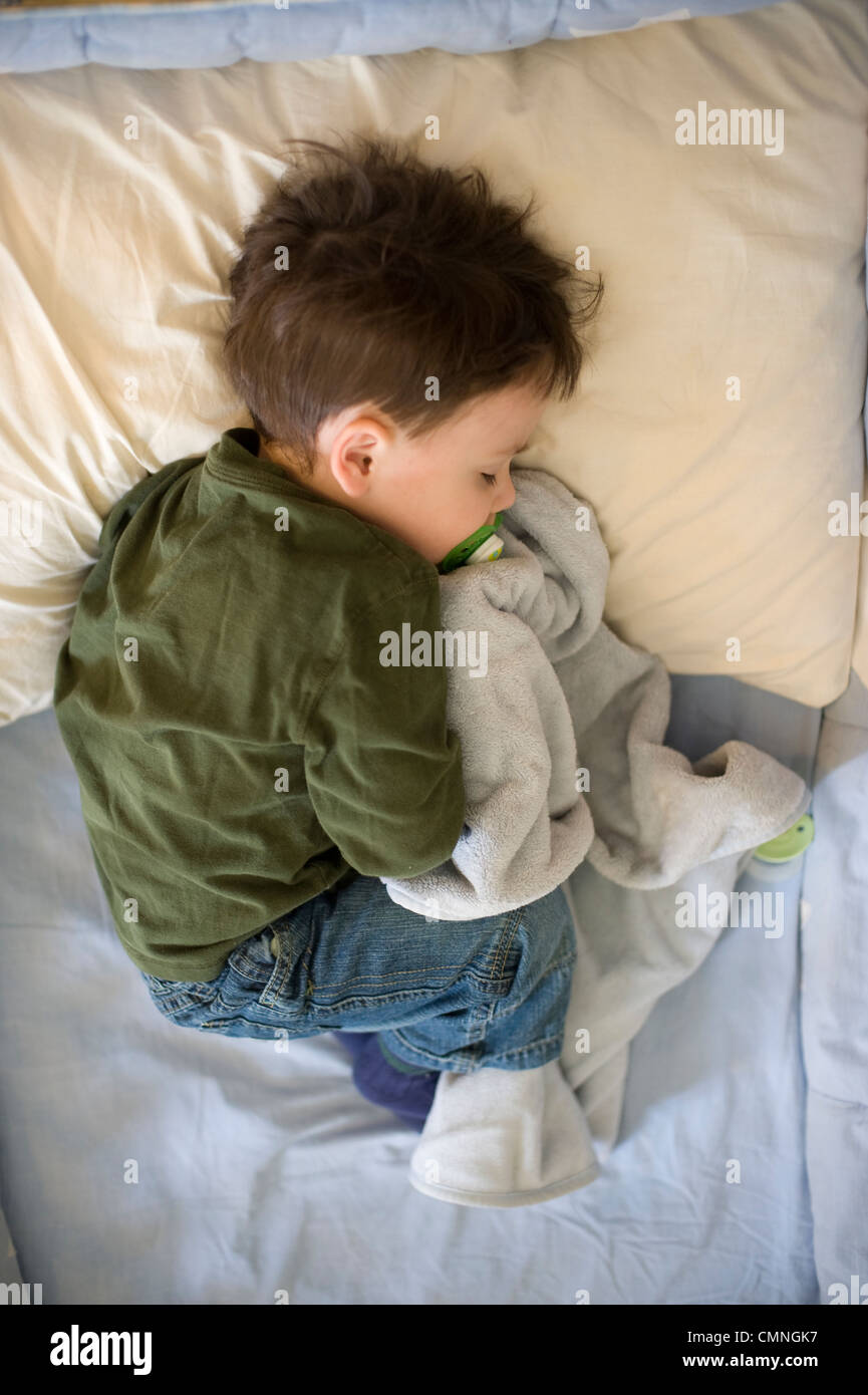 Two and 1/2 year old boy clutches his favorite blanket as he takes a nap in his crib Stock Photo