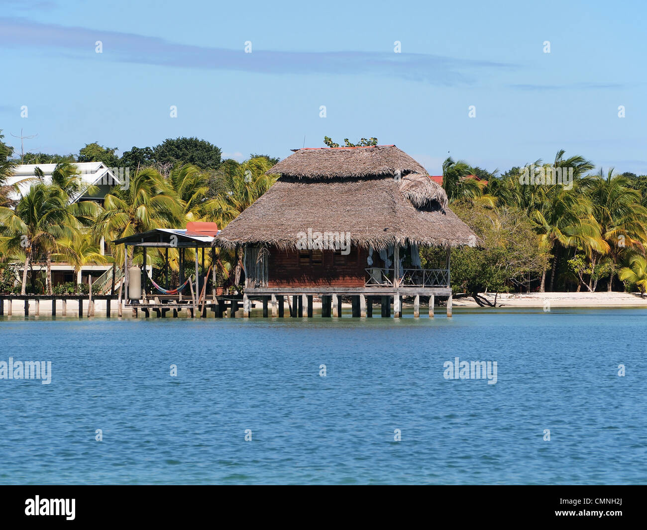 Bungalow on stilts with thatched roof over water and tropical beach in background, Bastimentos island, Caribbean side of Panama, Central America Stock Photo
