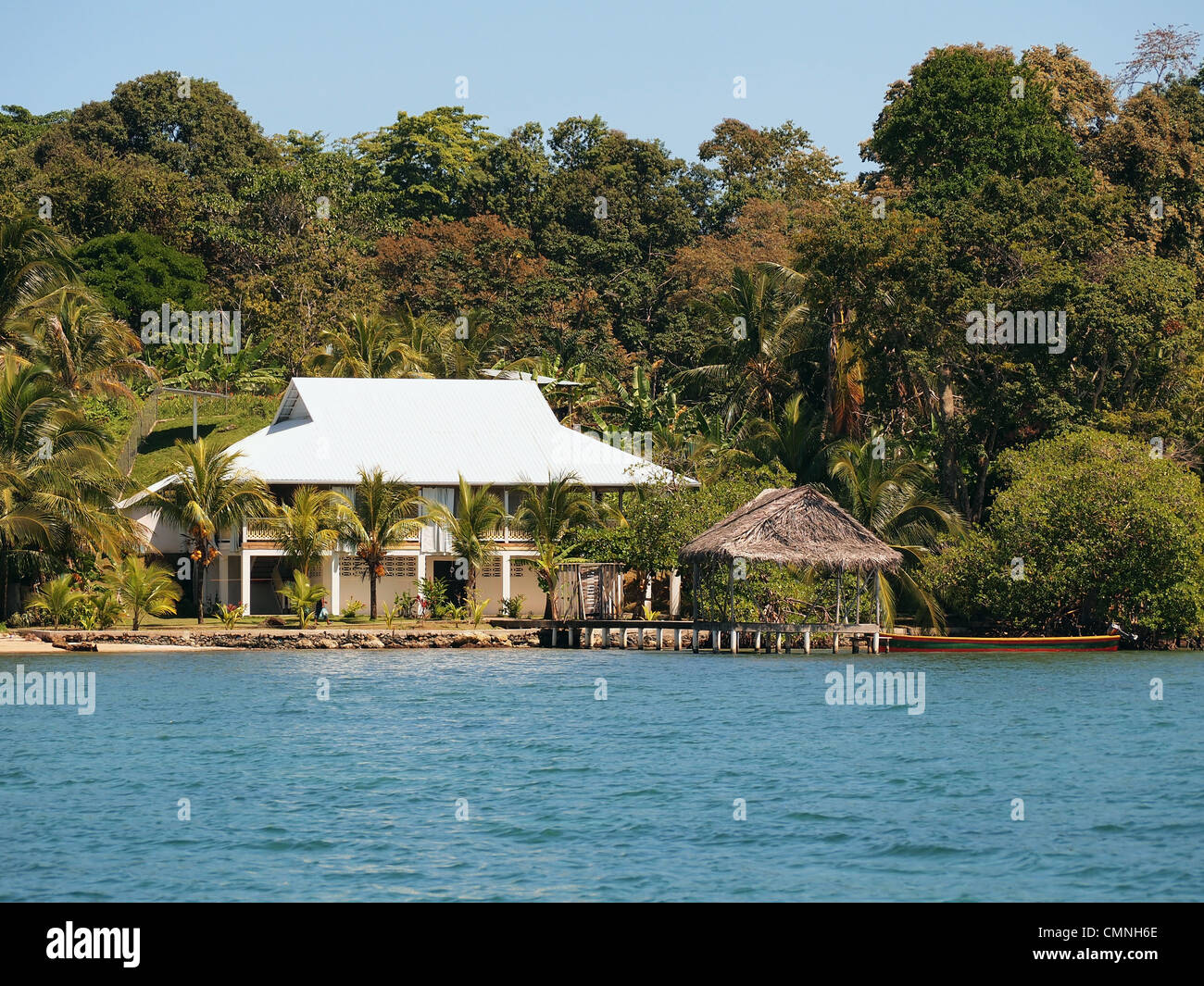 Waterfront tropical house on the shore with palm trees and a palapa over the sea, Central America, Panama Stock Photo