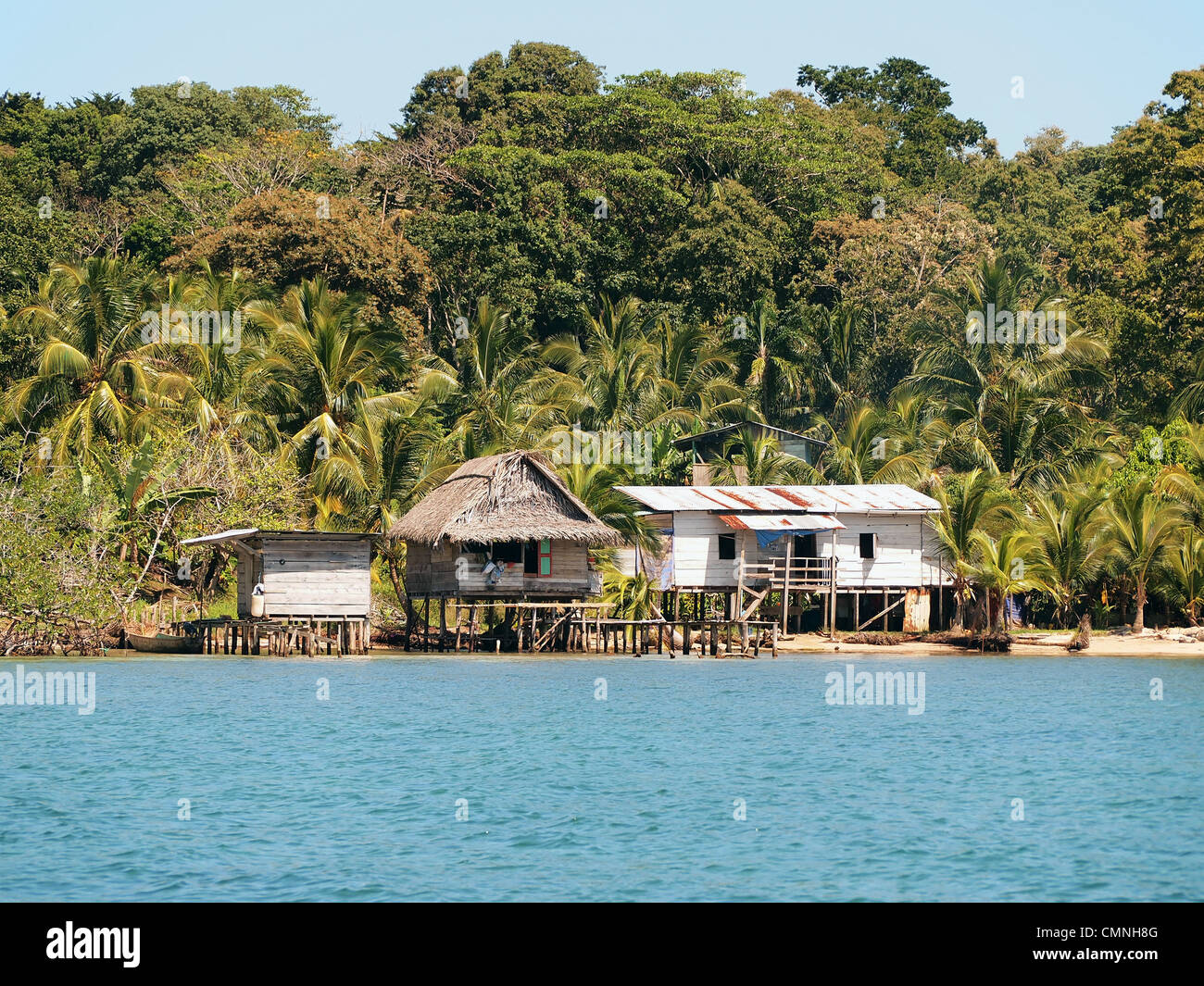 Rustic houses on stilts on the sea shore with lush tropical vegetation in background, Bocas del Toro, Panama, Central America Stock Photo