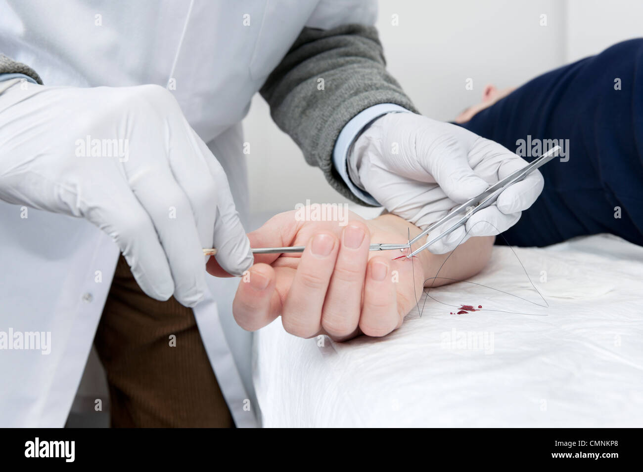 Doctor, wearing latex gloves, using a sterile needle and thread to stitch a nasty cut in a patients hand Stock Photo
