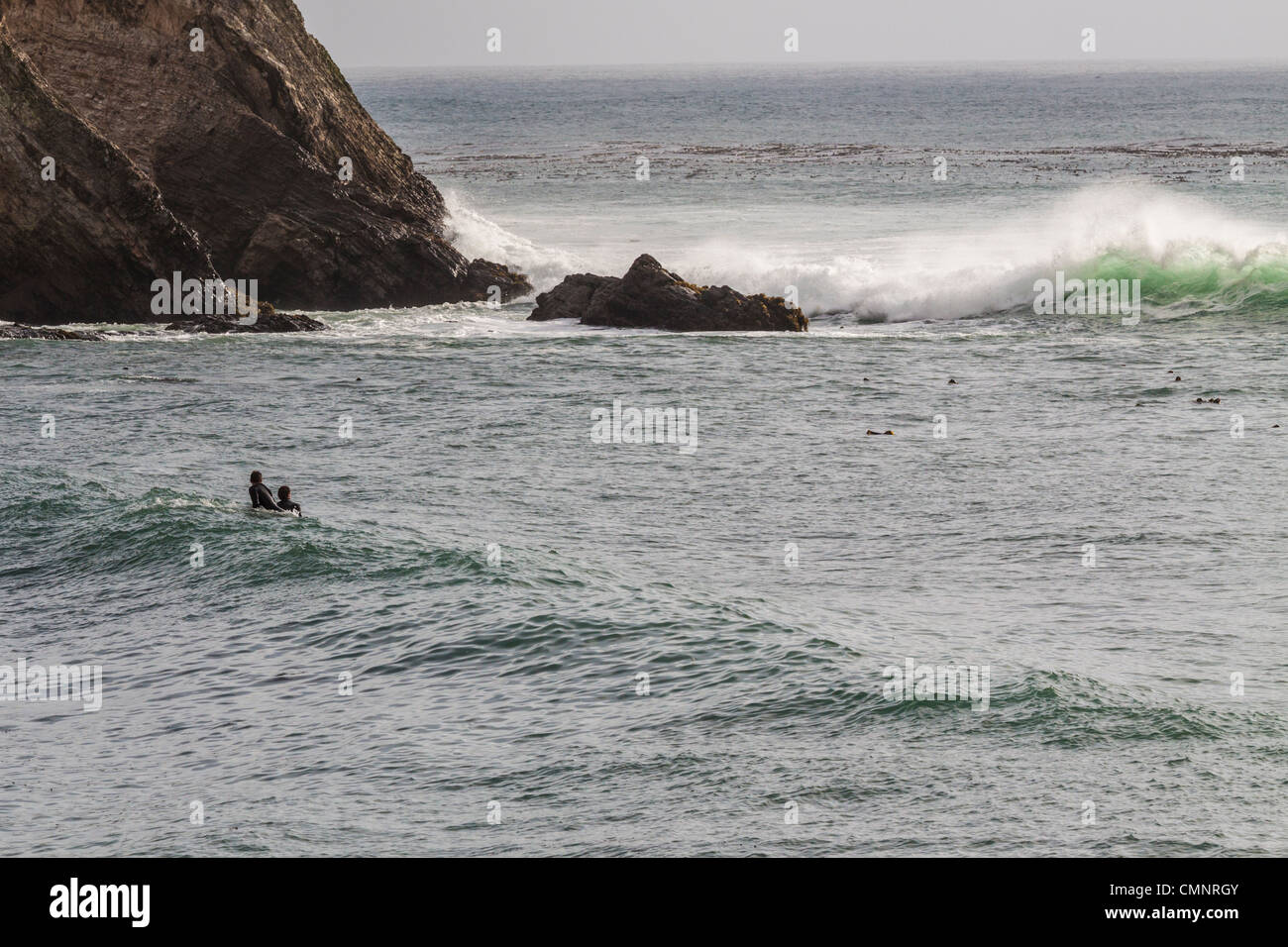 Stormy weather and surfers waiting for a wave in Pacific Ocean at Point Arena Pier inlet on Northern California coast. Stock Photo