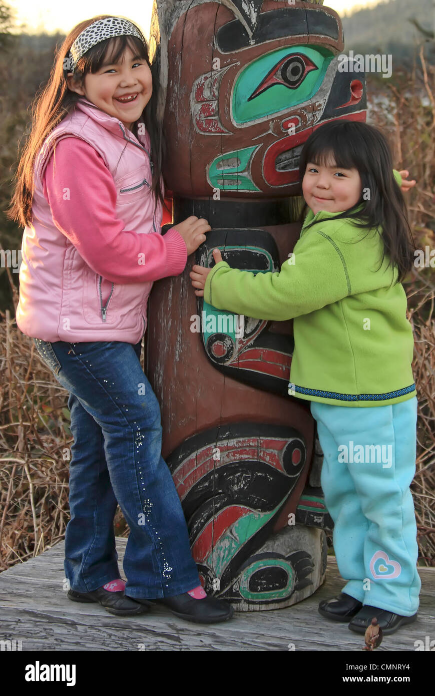Portrait of young First Nation girls hugging a totem pole, Vancouver Island, British Columbia Stock Photo