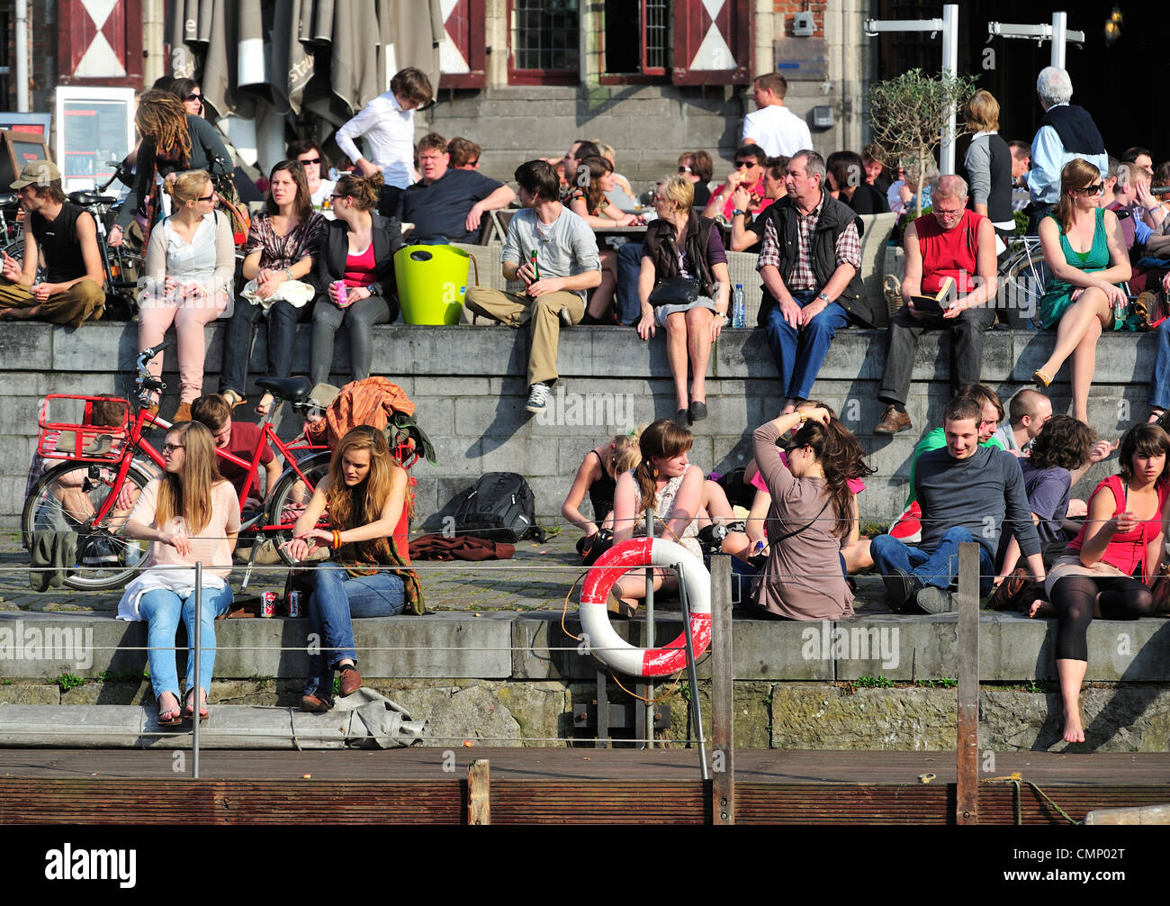 Tourists and students enjoying the first spring sun by the waterside along the Graslei at Ghent, Belgium Stock Photo