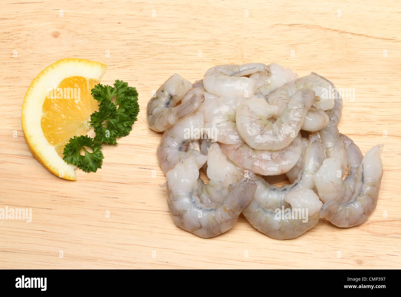 Raw king prawns and a wedge of lemon and parsley on a wooden board Stock Photo