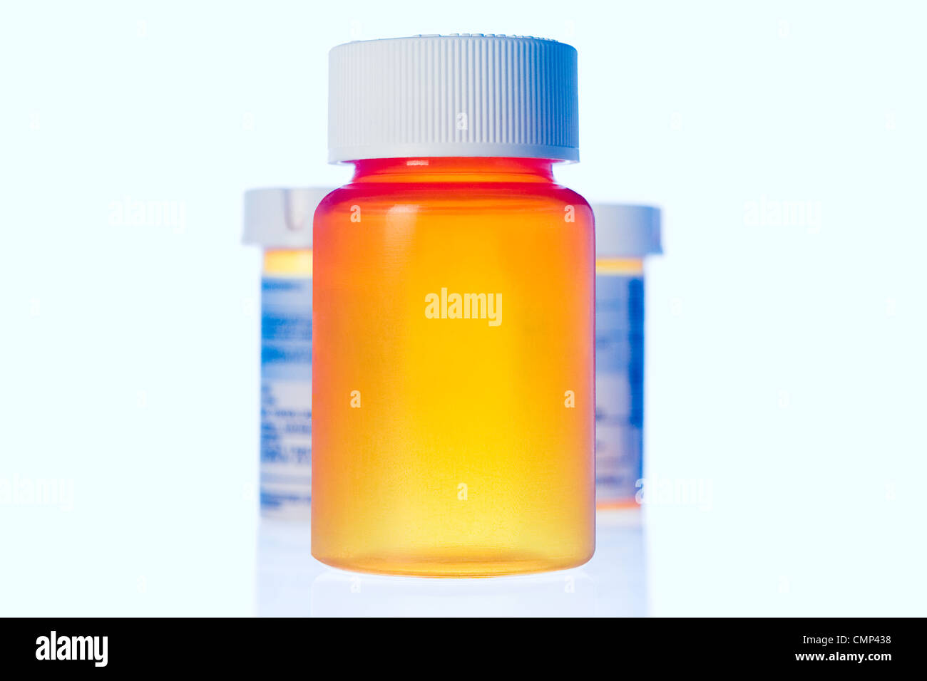 Three upright orange pill bottles in powder blue light on transparent surface. Large foreground empty bottle. Stock Photo