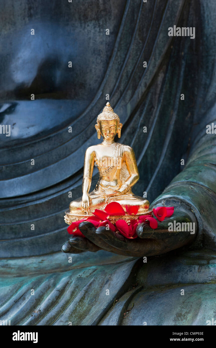 Golden Buddha statue and red rose petals on the hand of a very large buddha statue Stock Photo