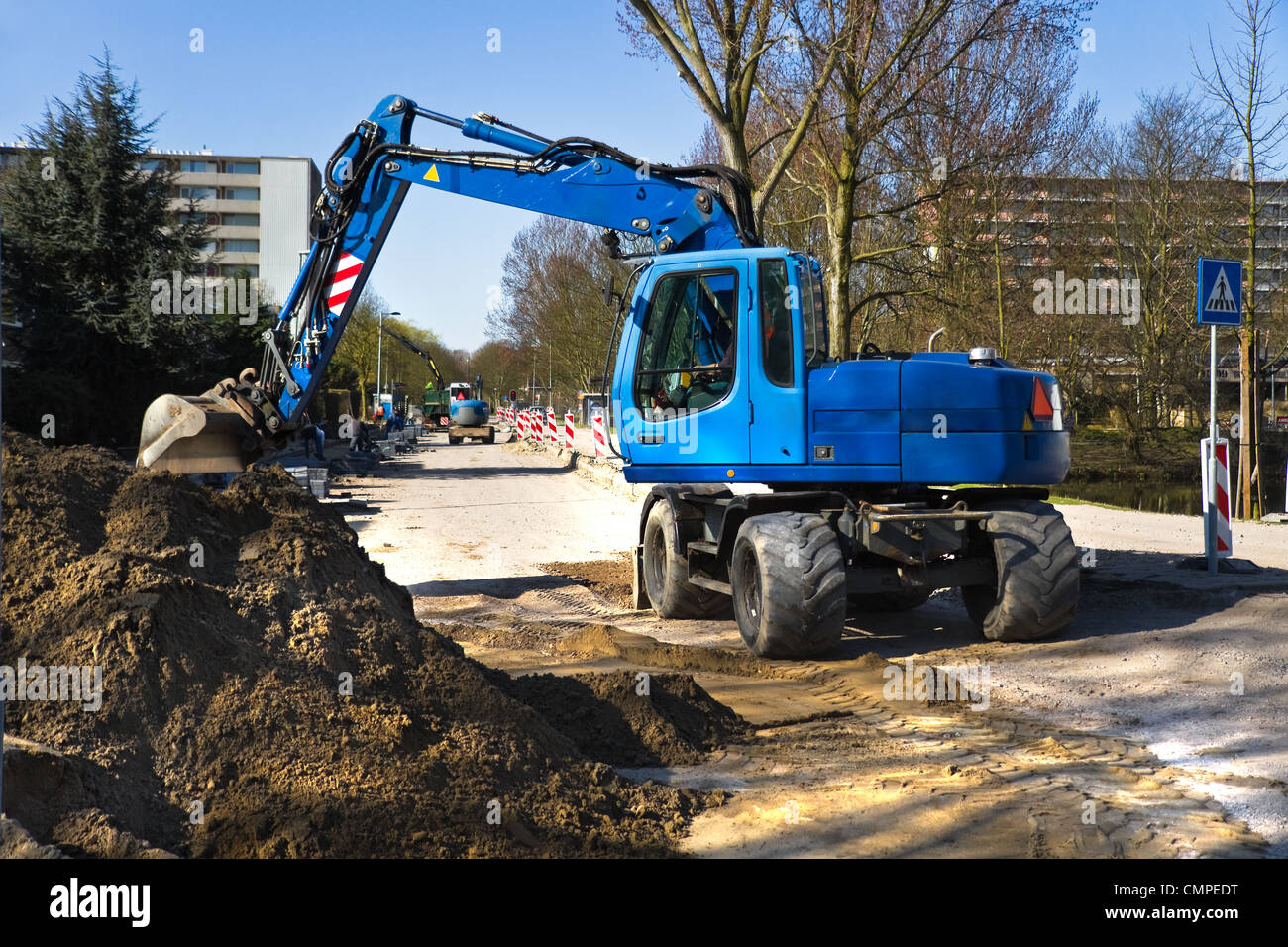Draglines at work to renew the pavement of a road in the city. Blue excavators and bright blue sky in early spring. Stock Photo