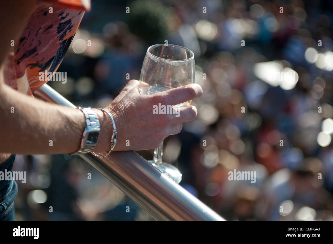 A woman's hand holds a partly empty wine glass over a railing over a beer garden on a sunny day. Stock Photo