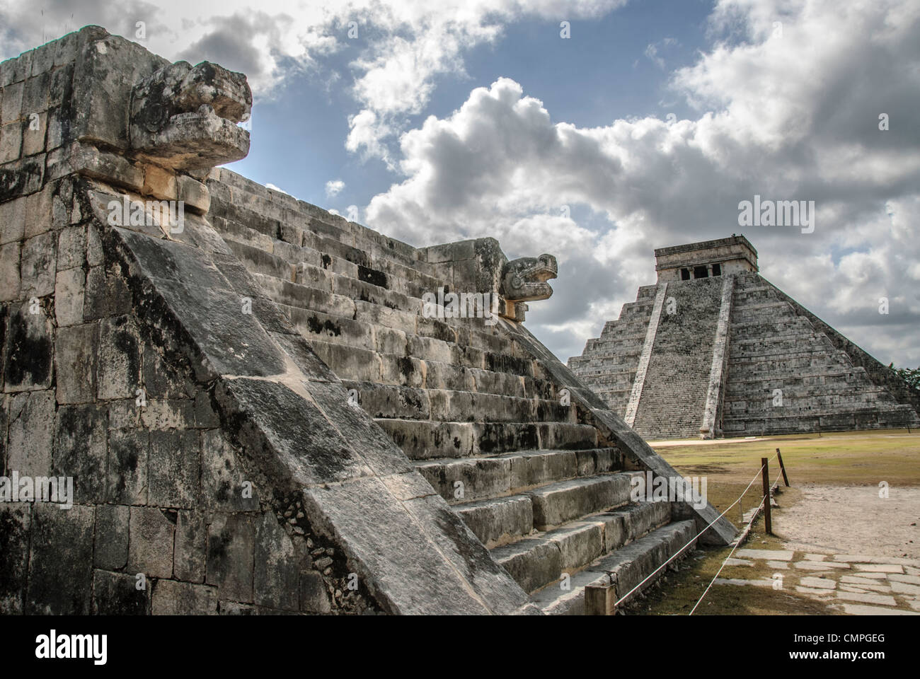 CHICHEN ITZA, Mexico - In the background at right is the Temple of Kukulkan (El Castillo) and at left in the foreground are the carved jaguar heads of the Venus Platform at Chichen Itza Archeological Zone, ruins of a major Maya civilization city in the heart of Mexico's Yucatan Peninsula. Stock Photo