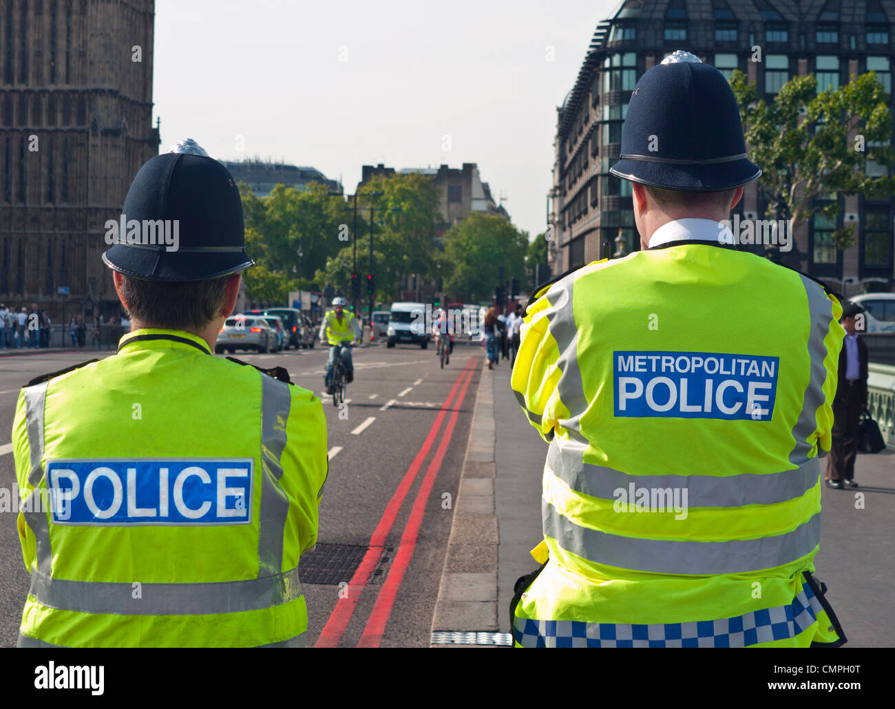 LONDON Metropolitan Police officers back view wearing tabards on duty at Westminster Bridge red route traffic lines Houses of Parliament London UK Stock Photo