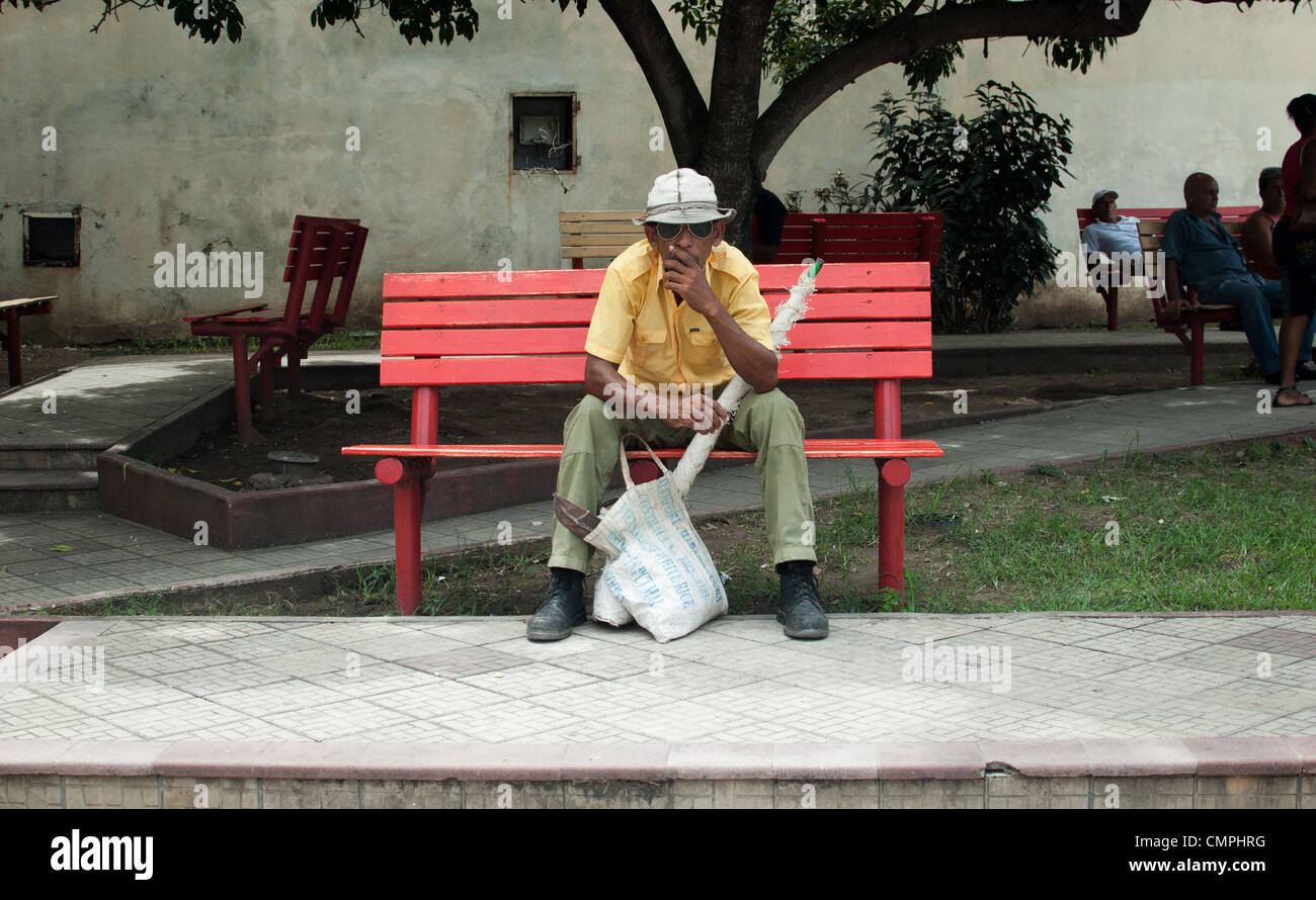 Cuban man sitting on the bench under a tree with packages Stock Photo