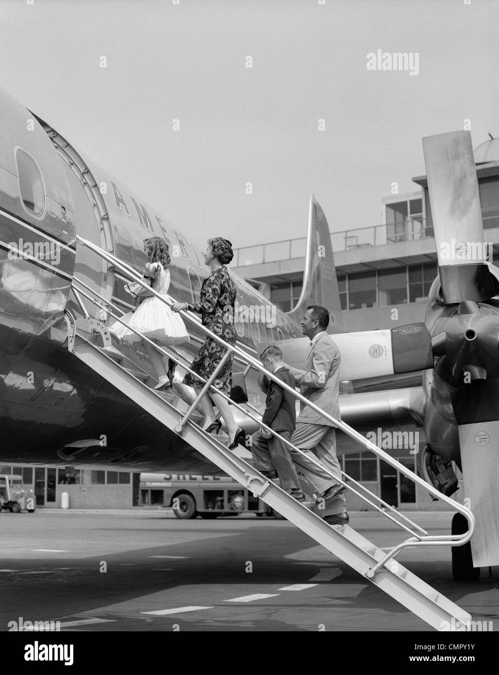 1950s FAMILY FATHER MOTHER DAUGHTER SON BOARDING PROPELLER AIRLINER BY CLIMBING GANGWAY STAIRS AT AIRPORT Stock Photo