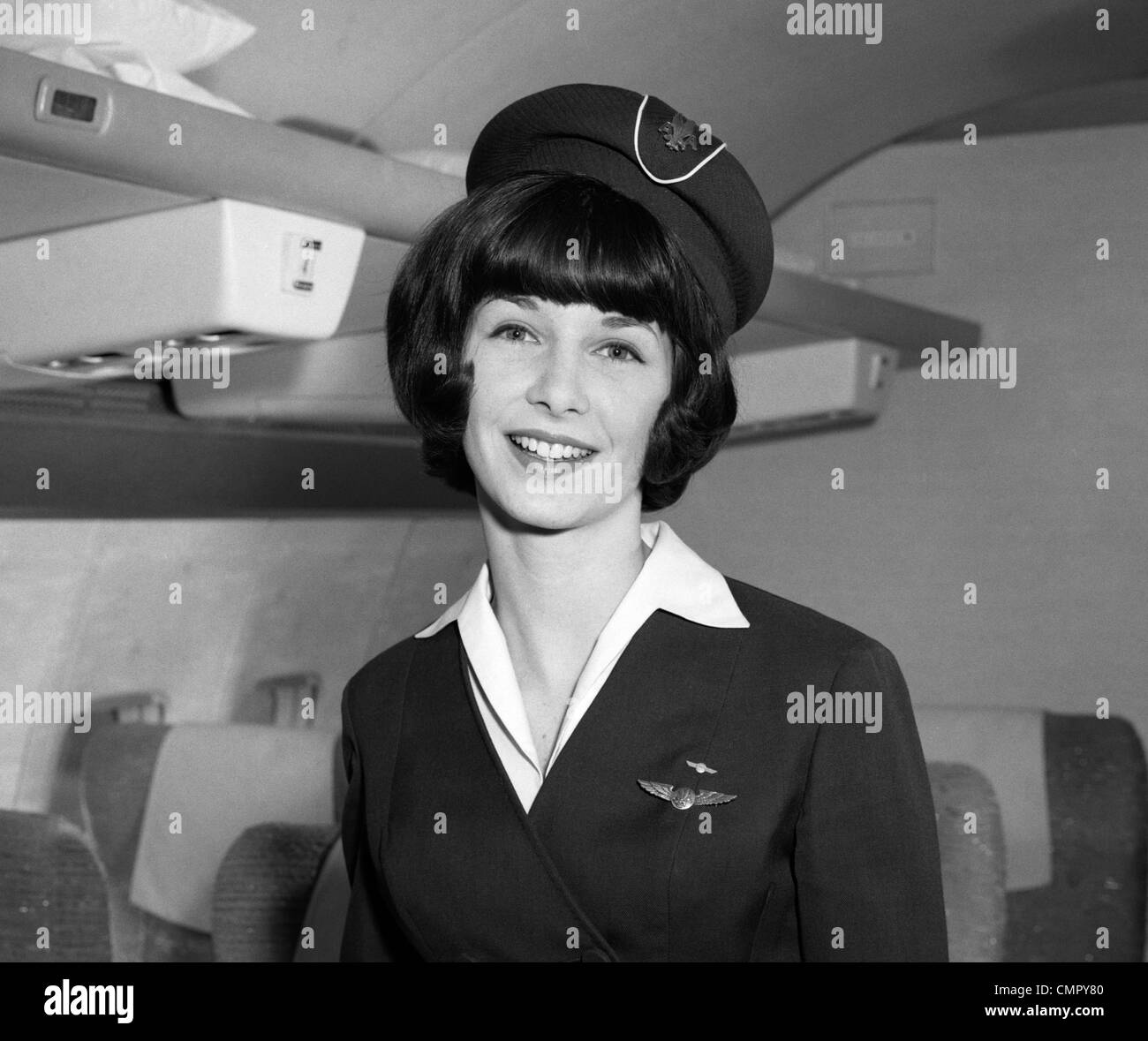 1960s SMILING PORTRAIT OF AIRLINE STEWARDESS IN AIRPLANE AISLE Stock Photo