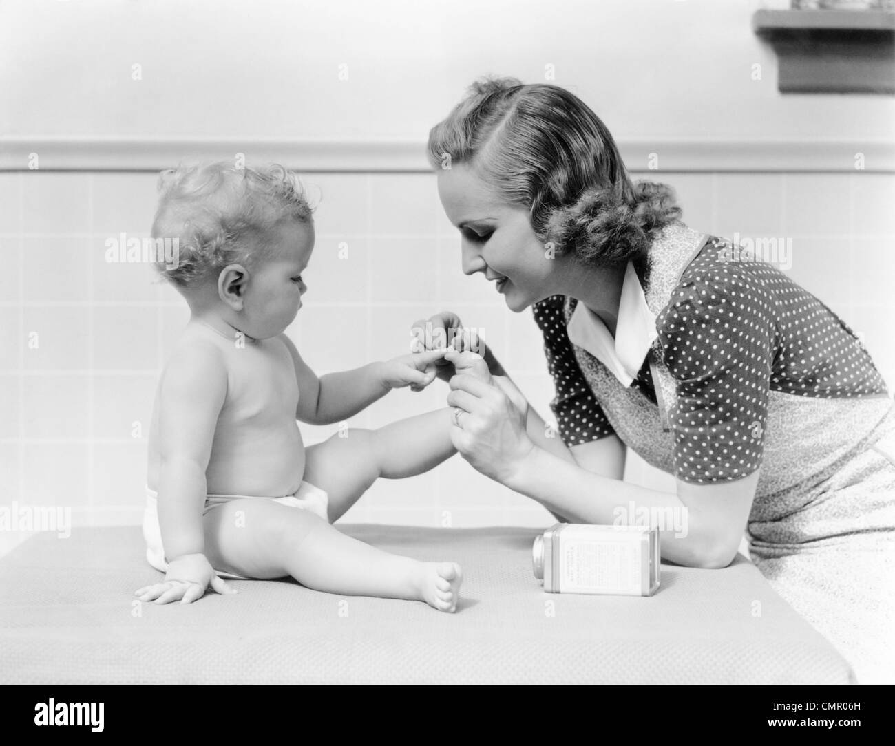 1930s MOTHER TOUCHING BABY TOES FINGERS THIS LITTLE PIGGY NURSERY RHYME Stock Photo