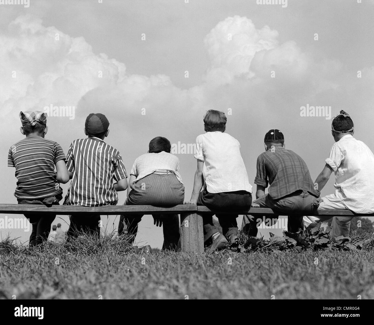 1960s BACK VIEW OF SIX BOY BASEBALL PLAYERS SITTING ON BENCH Stock Photo