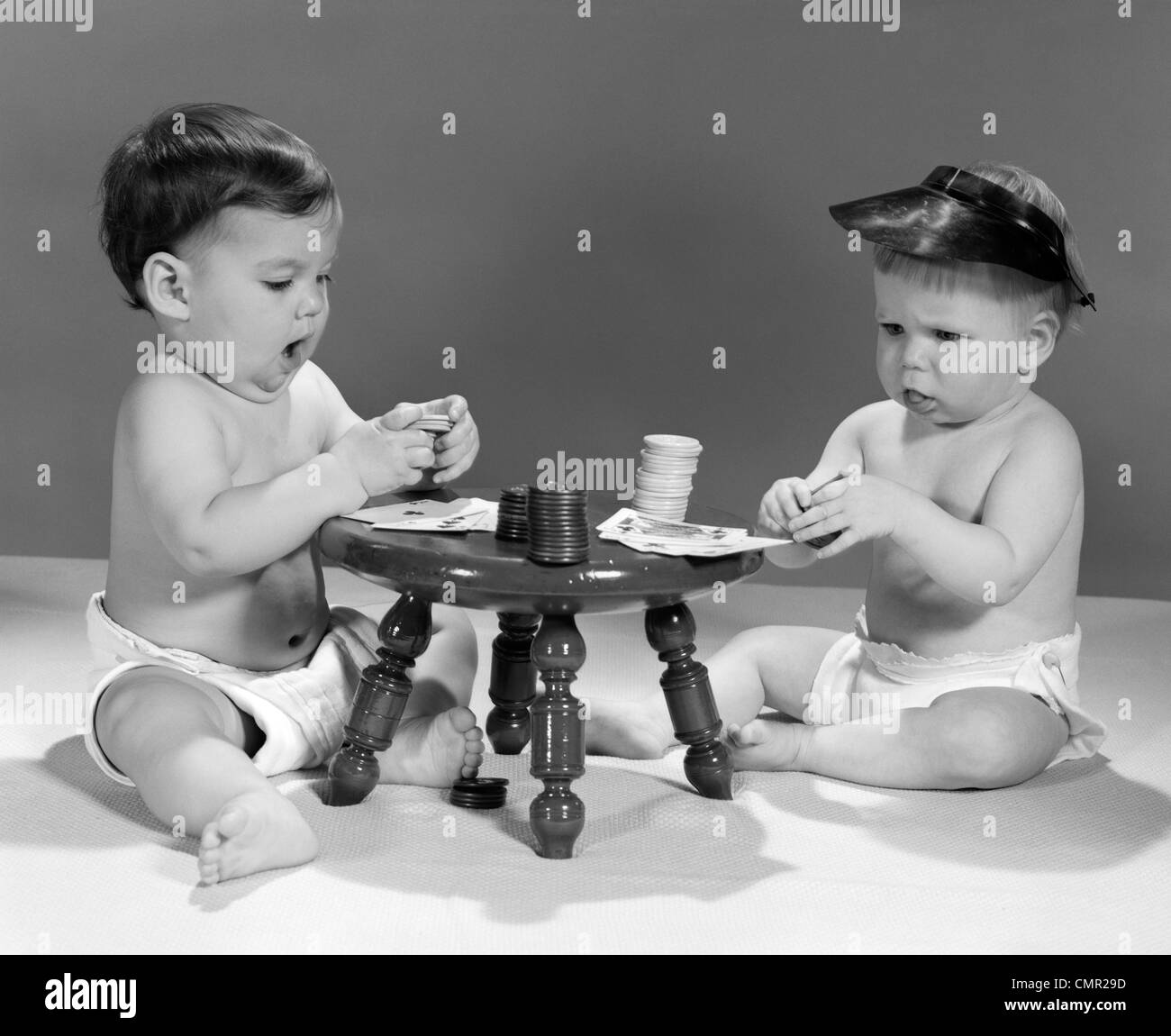1960s TWO BABIES IN DIAPERS PLAYING POKER CARDS WEARING VISORS Stock Photo