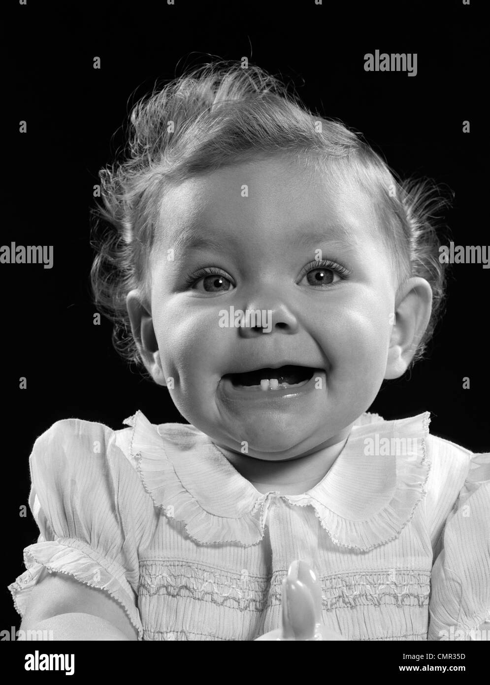 1950s PORTRAIT BABY GIRL SMILING WITH TWO BOTTOM TEETH SHOWING LOOKING AT CAMERA Stock Photo