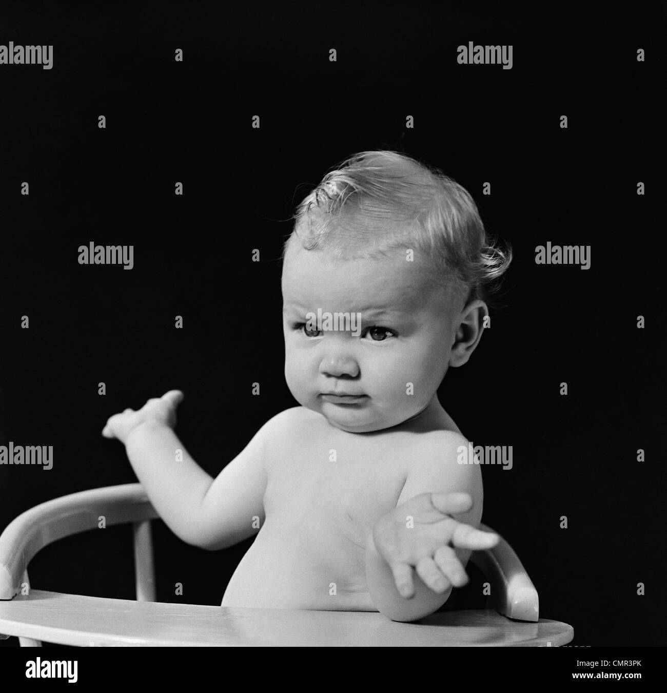 1930s 1940s BABY IN HIGH CHAIR MAKING SHRUGGING GESTURE Stock Photo