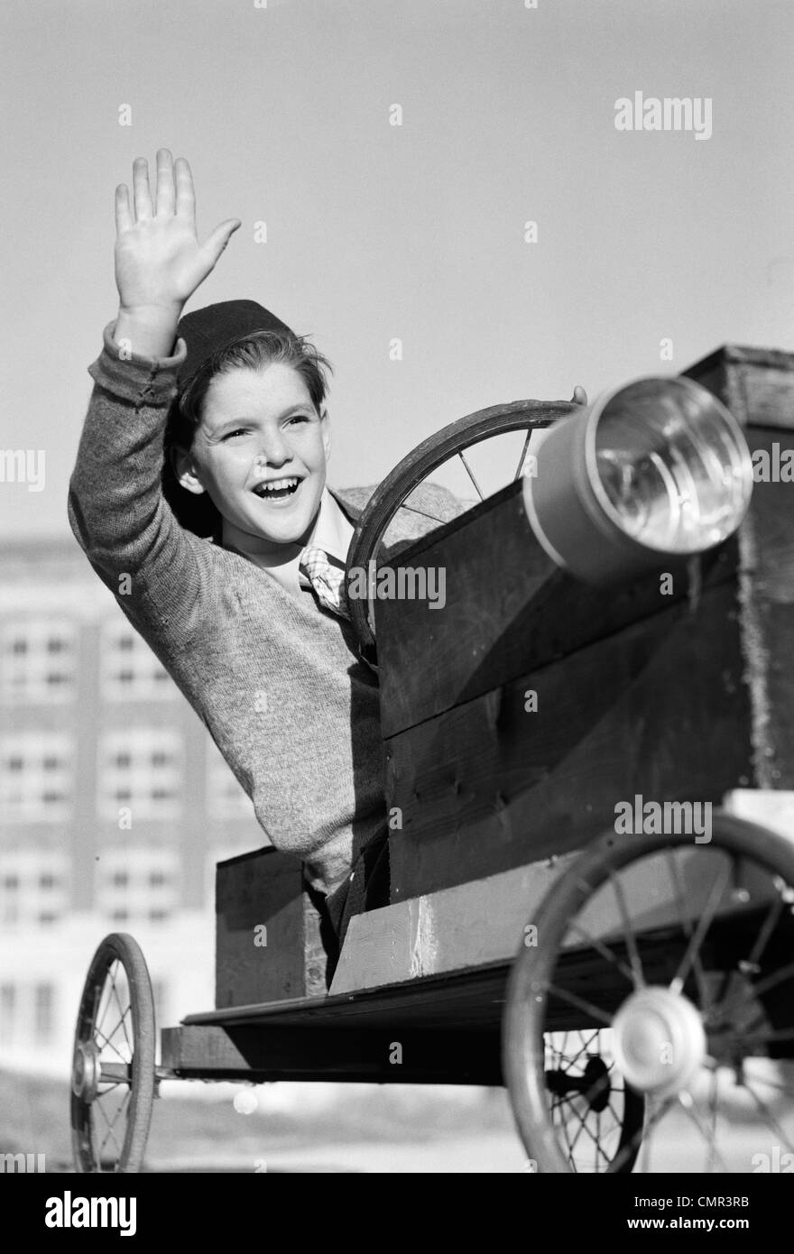 1940s BOY IN HOMEMADE RACE CAR GO-CART SMILING AND WAVING SOAPBOX DERBY Stock Photo