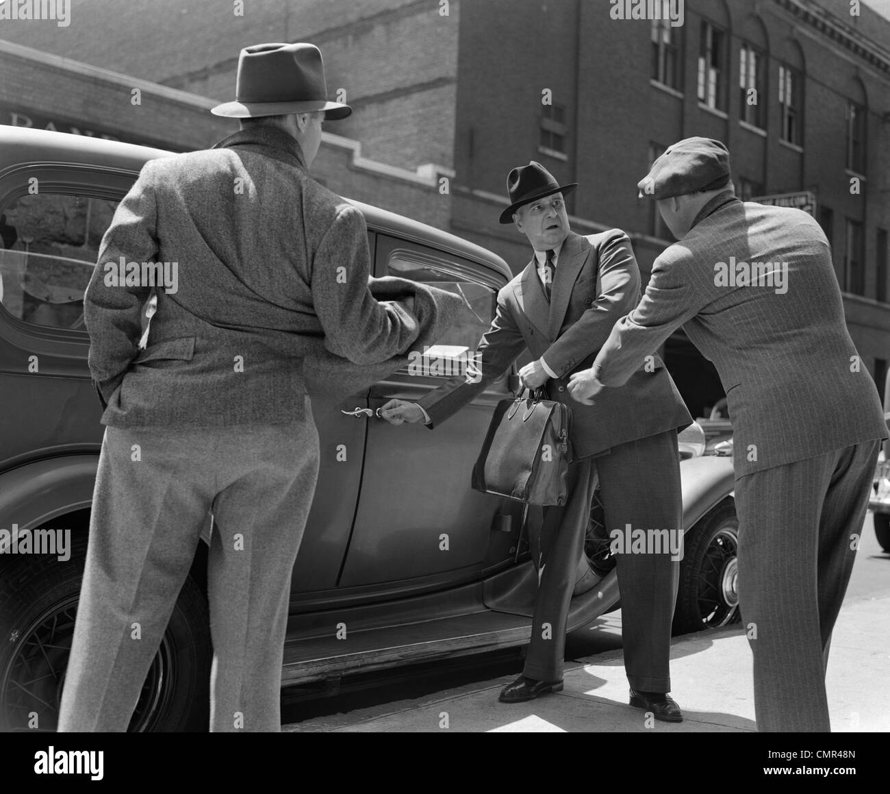 1940s PAIR OF GANGSTERS HOLDING UP MAN GETTING INTO CAR WITH BRIEFCASE Stock Photo