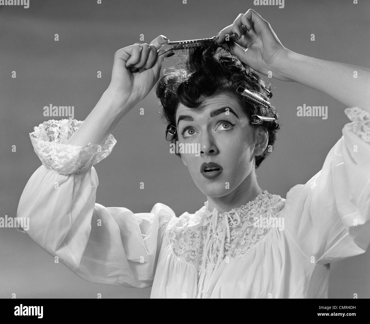 1950s WOMAN IN NIGHTGOWN PUTTING ROLLER CLIPS IN HAIR Stock Photo