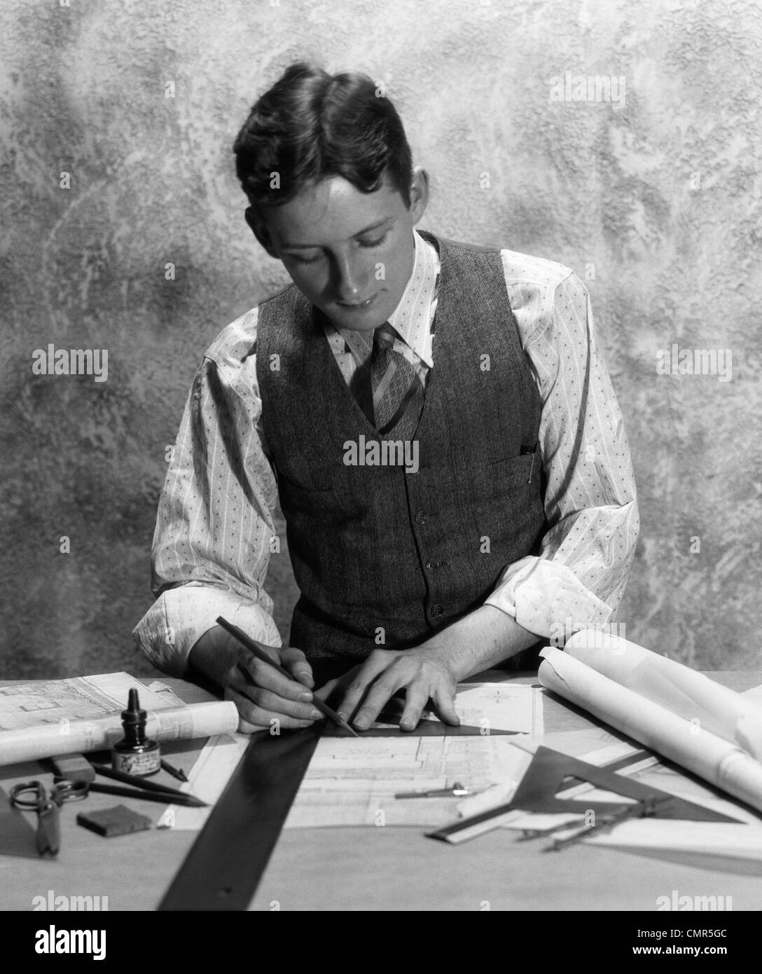 1920s 1930s YOUNG MAN AT DESK DRAFTING WITH TRIANGLE & STRAIGHT EDGE Stock Photo