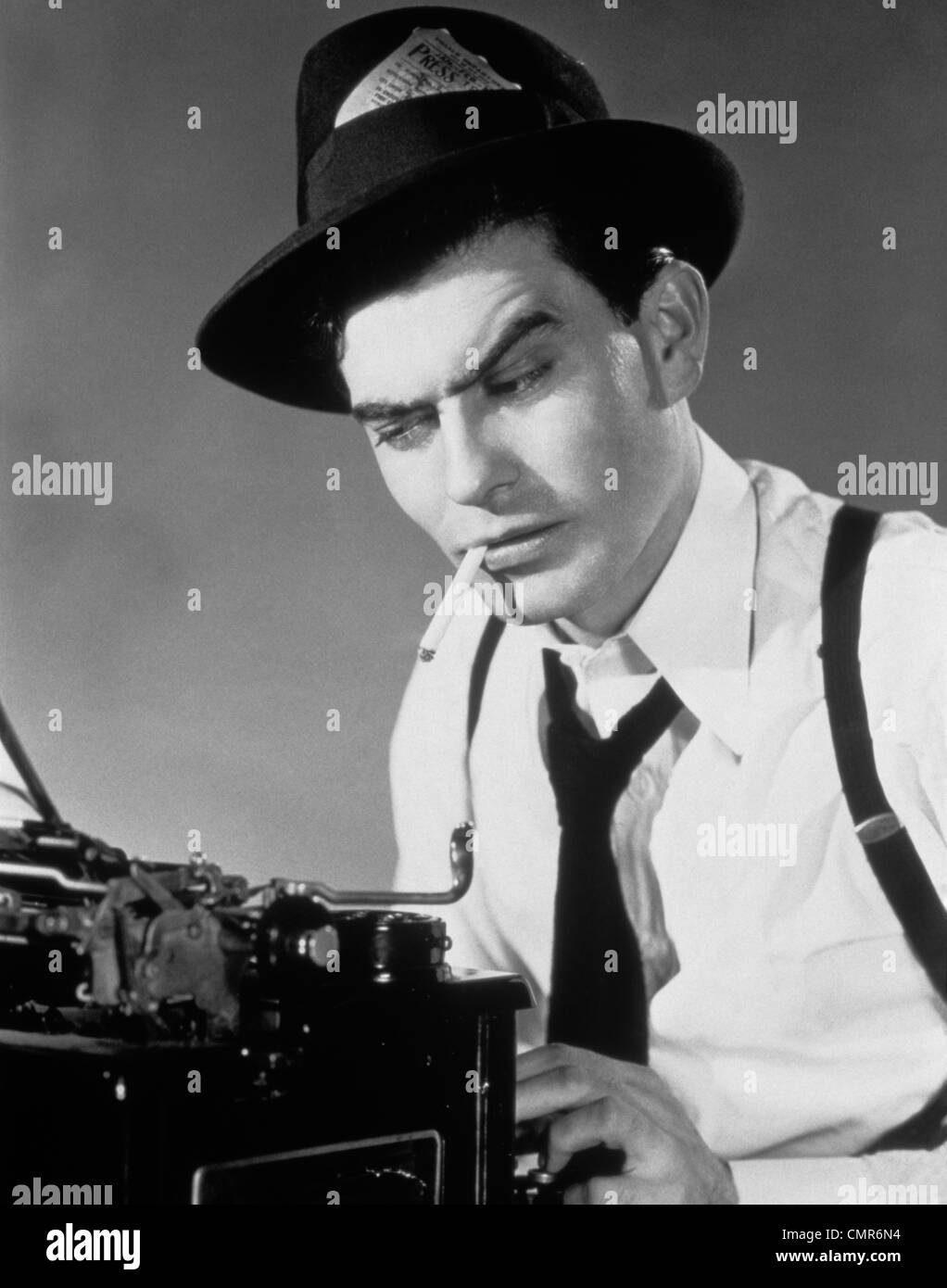 1940s 1950s MAN REPORTER SITTING AT TYPEWRITER SMOKING CIGARETTE PRESS PASS IN HATBAND Stock Photo