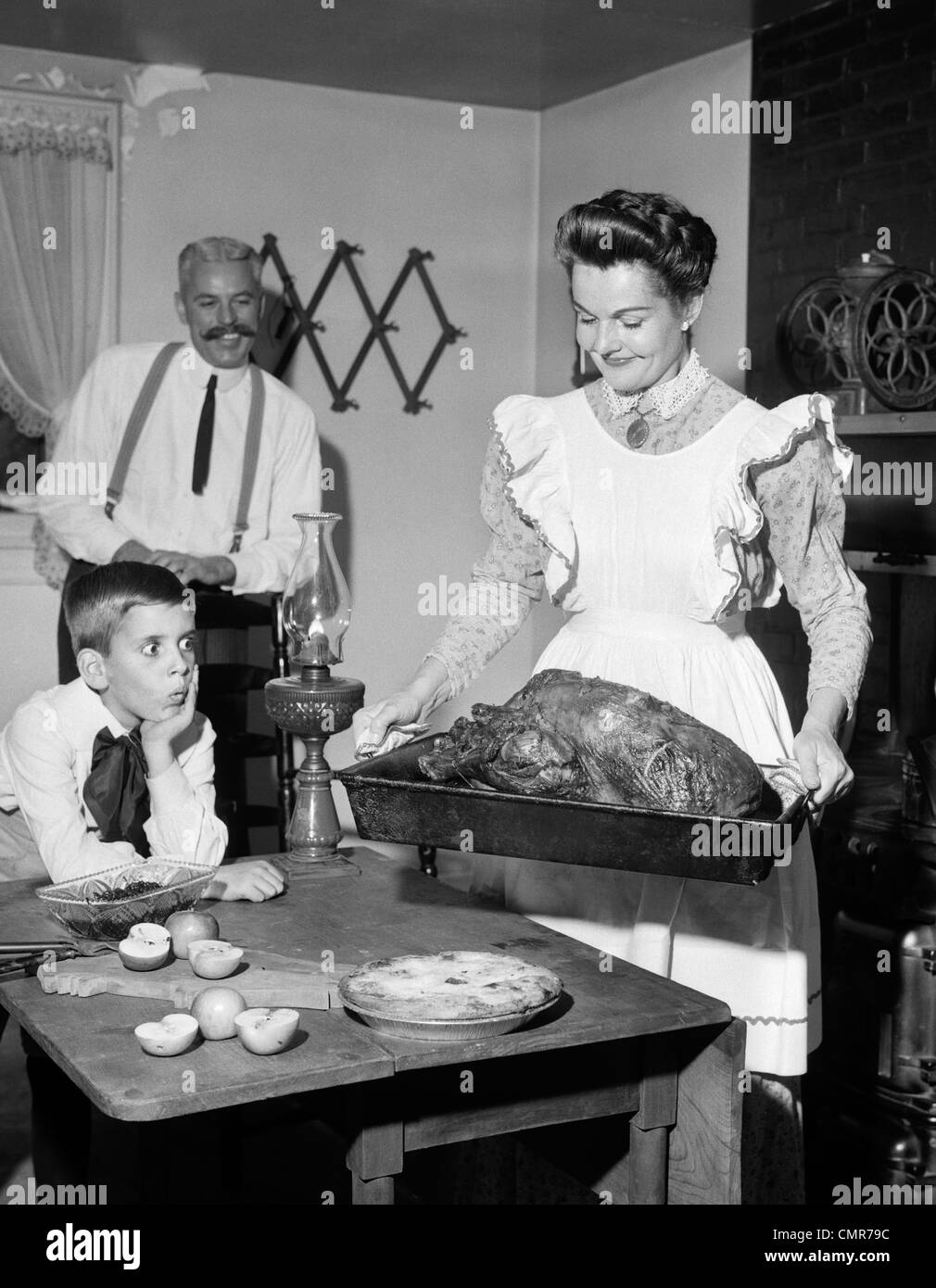 1950s MOCK TURN OF THE 20TH CENTURY THANKSGIVING DINNER SMILING MOTHER SHOWING ROAST TURKEY TO PLEASED HUSBAND AND SURPRISED Stock Photo