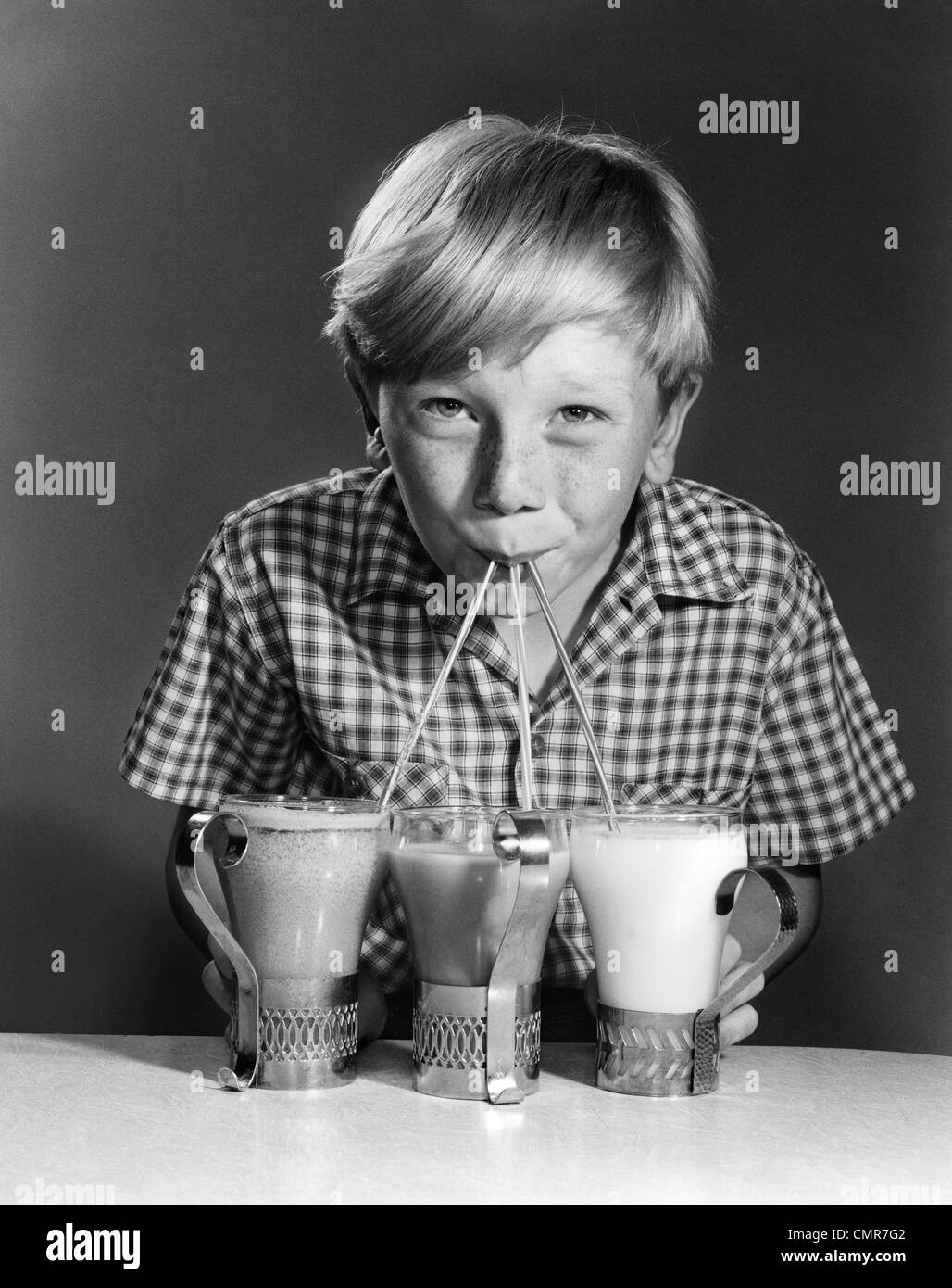 1950s 1960s PORTRAIT OF BLONDE BOY DRINKING WITH STRAWS FROM 3 MILKSHAKES SODAS SMILING LOOKING AT CAMERA Stock Photo