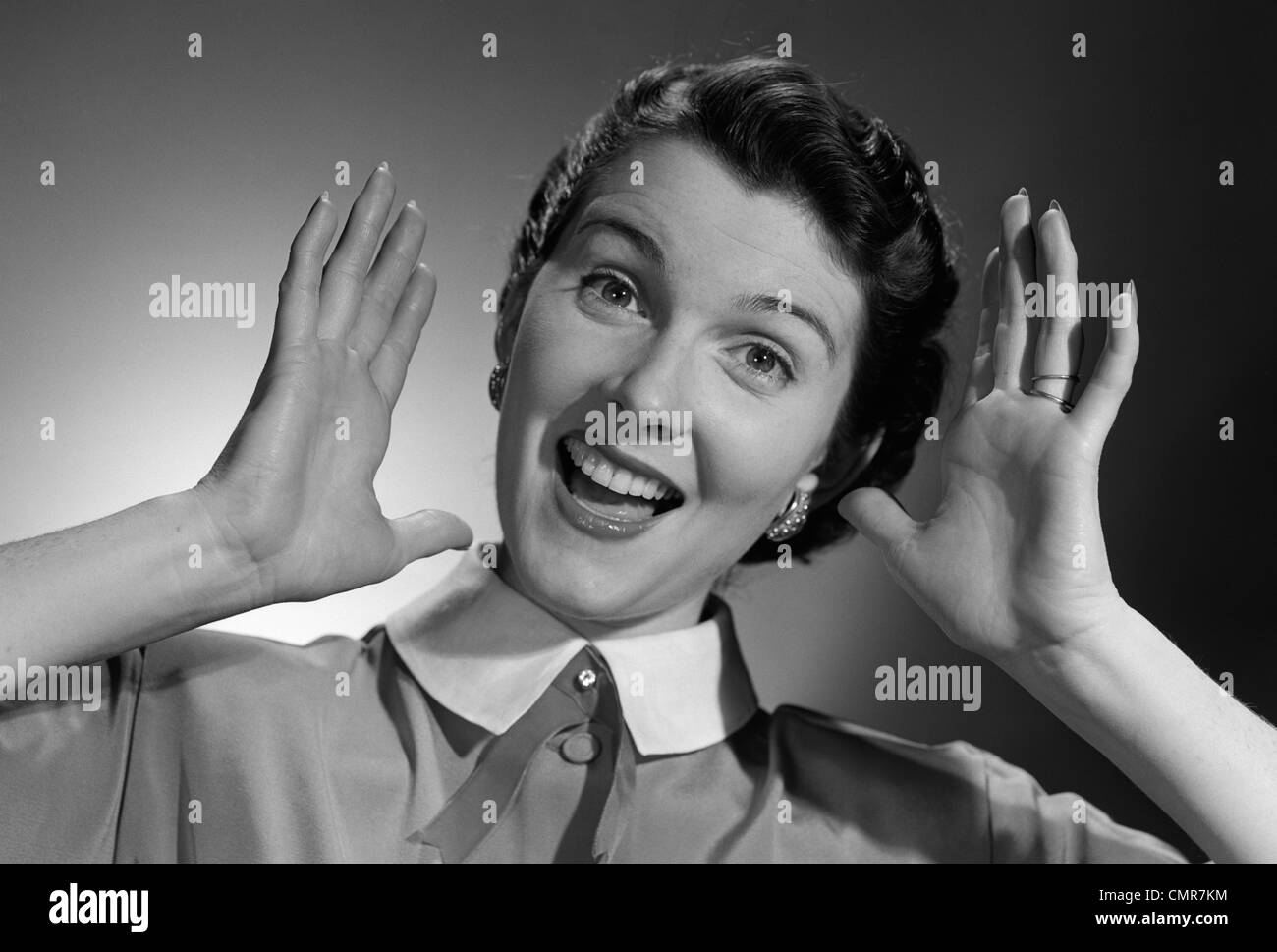 1950s SMILING HAPPY WOMAN HOLDING HANDS UP BESIDE HER HEAD Stock Photo