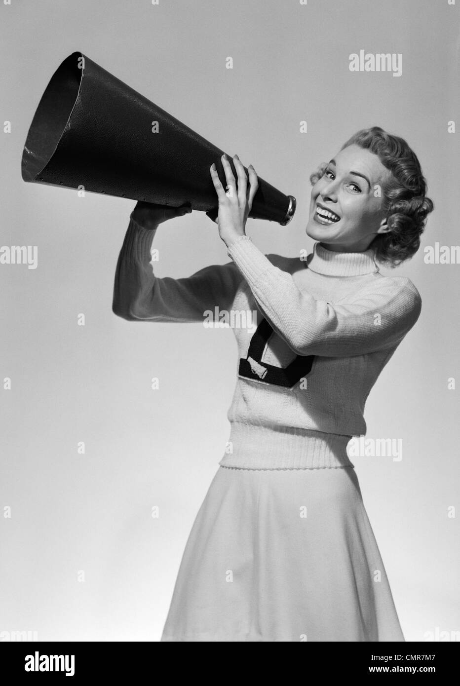 1950s PORTRAIT SMILING TEENAGE GIRL CHEERLEADER IN SWEATER AND LONG SKIRT CHEERING THROUGH MEGAPHONE LOOKING AT CAMERA Stock Photo