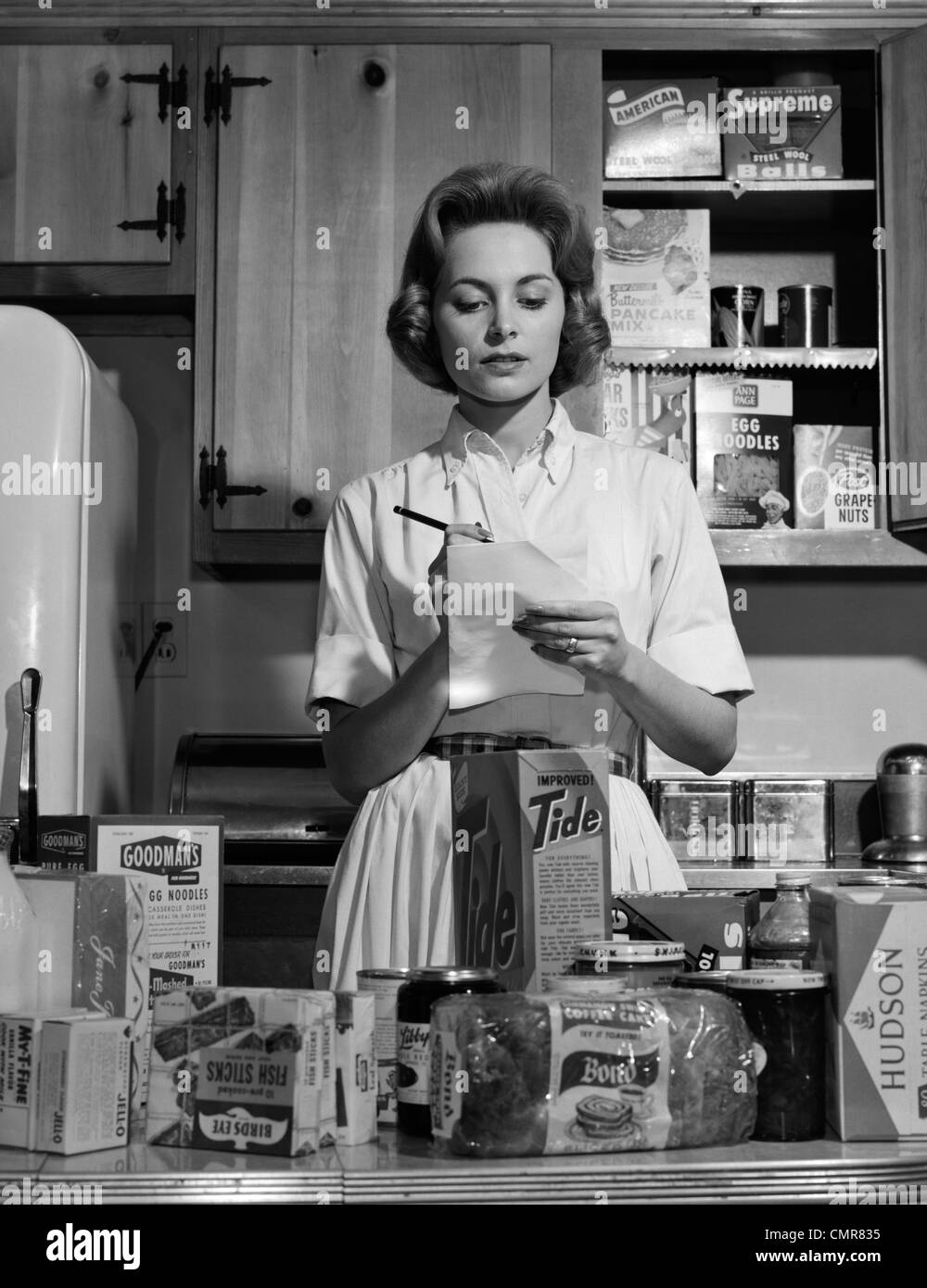 1960s WOMAN HOUSEWIFE IN KITCHEN CHECKING GROCERY FOOD SHOPPING LIST Stock Photo