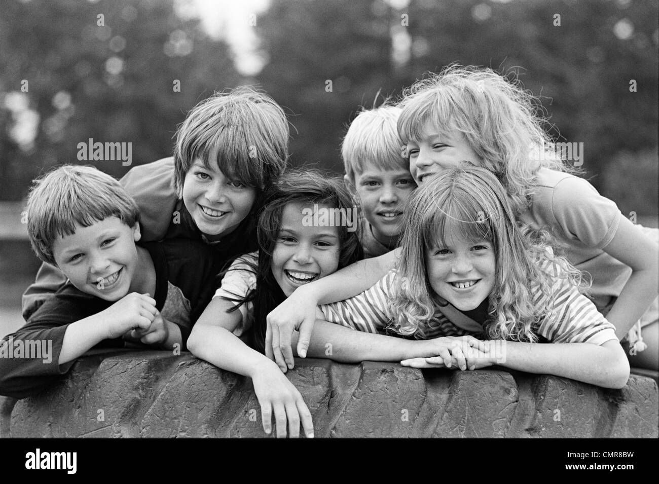 1970s 1980s GROUP OF SIX BOYS & GIRLS GATHERED TOGETHER ON LARGE PLAYGROUND TIRE Stock Photo